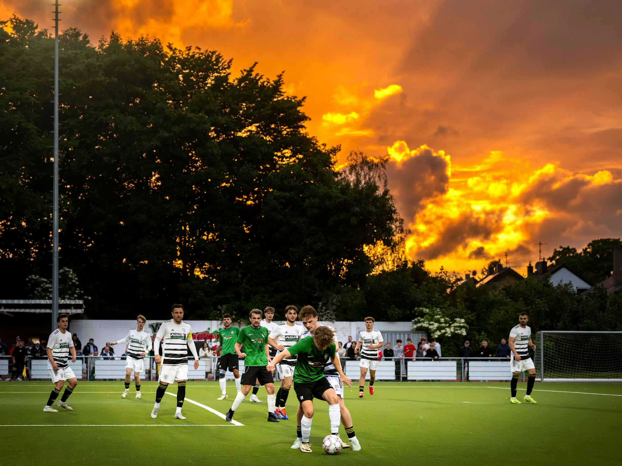 Ein Fußballspiel findet vor einem Sonnenuntergang statt, der den Himmel orange gefährt hat.