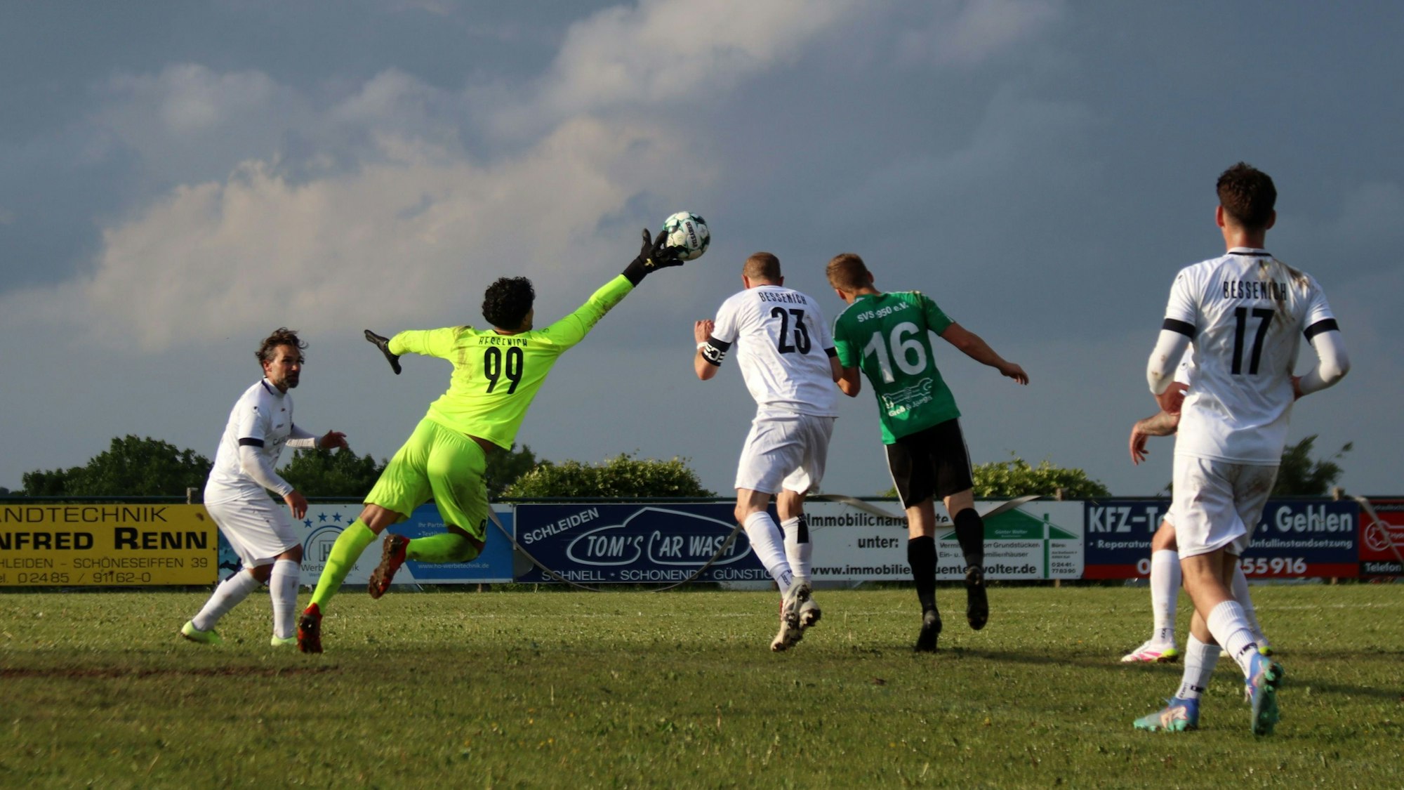 Ein Fußball-Torwart streckt sich und kann den Ball mit den Fingerspitzen abwehren, dahinter wäre es zu einem Kopfballduell zweier Spieler gekommen.