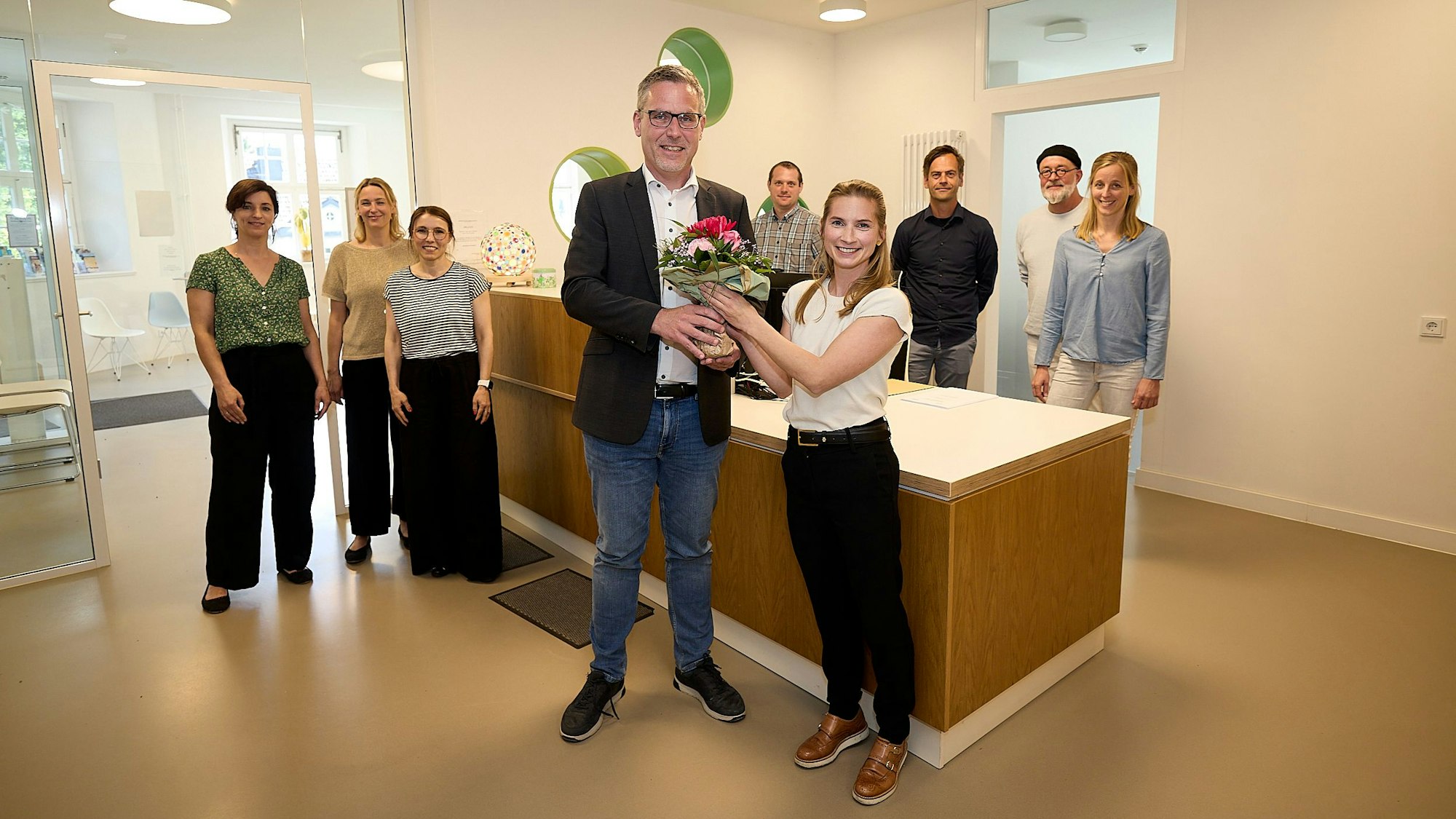 Das Team des Ärztezentrums Nettersheim steht im Hintergrund. Vorne überreicht Bürgermeister Norbert Crump Blumen an Caroline Lenz, die das Team als Gynäkologin verstärken wird.