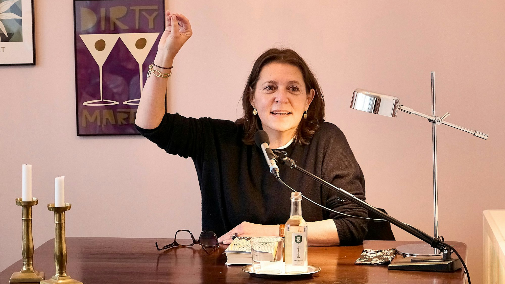 Die Kölner Autorin und Journalistin Husch Josten sitzt vor einem Tisch mit einem Mikro und gestikuliert mit der rechten Hand.