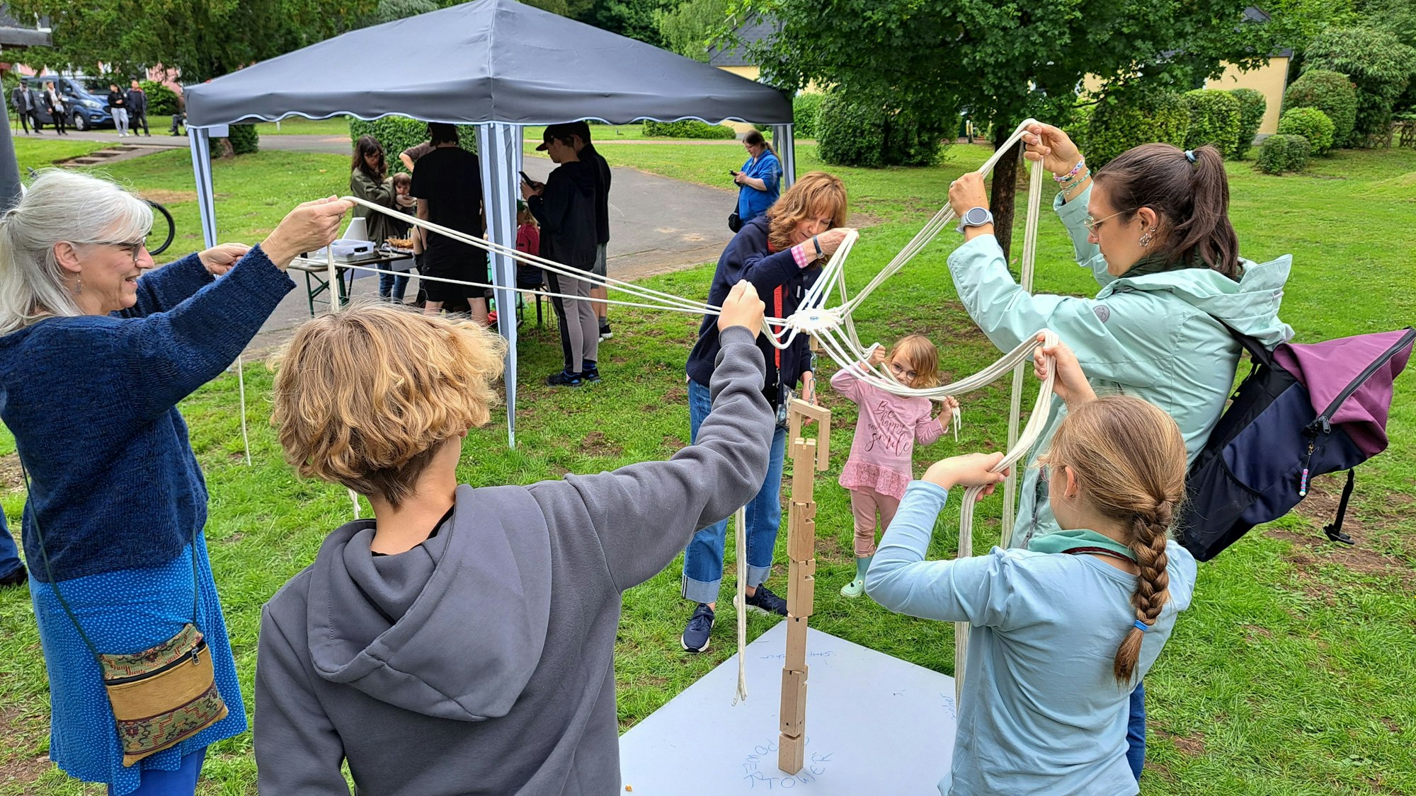 Erwachsene und Kinder spielen ein Kooperationsspiel, bei dem sie die Enden von zusammenhängenden Schnüren halten.
