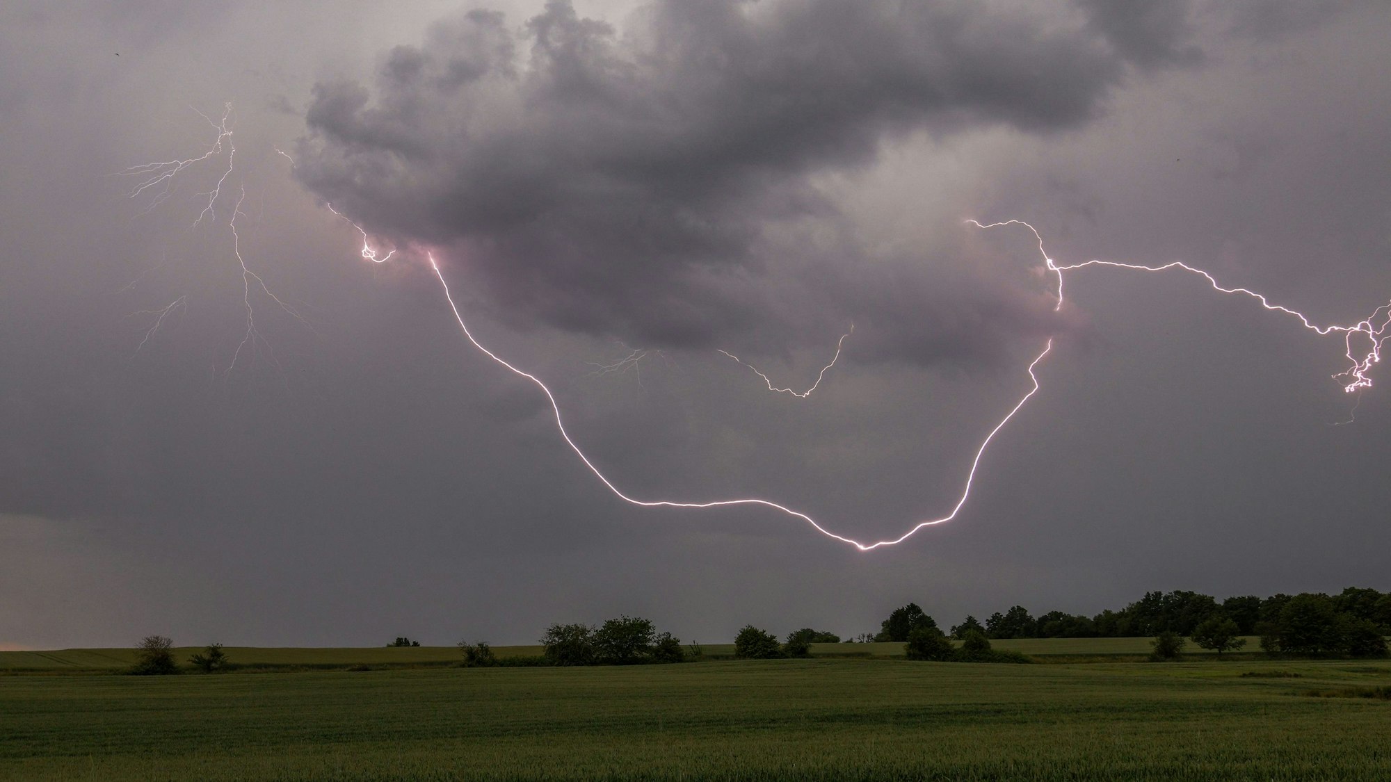 Blitze eines Gewitters erhellen die dunklen Wolken über der Landschaft. In NRW toben am Wochenende schwere Gewitter, warnt der Deutsche Wetterdienst. (Symbolbild)