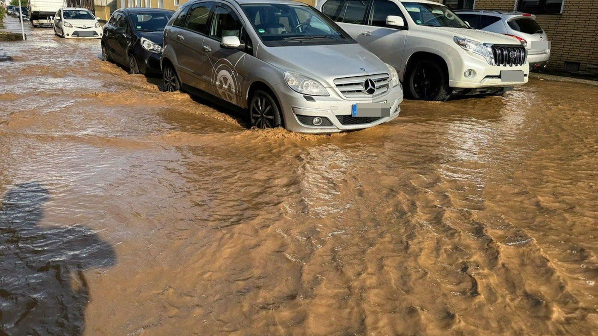 Das Bild zeigt mehrere Autos, die von Wassermassen umgeben sind.