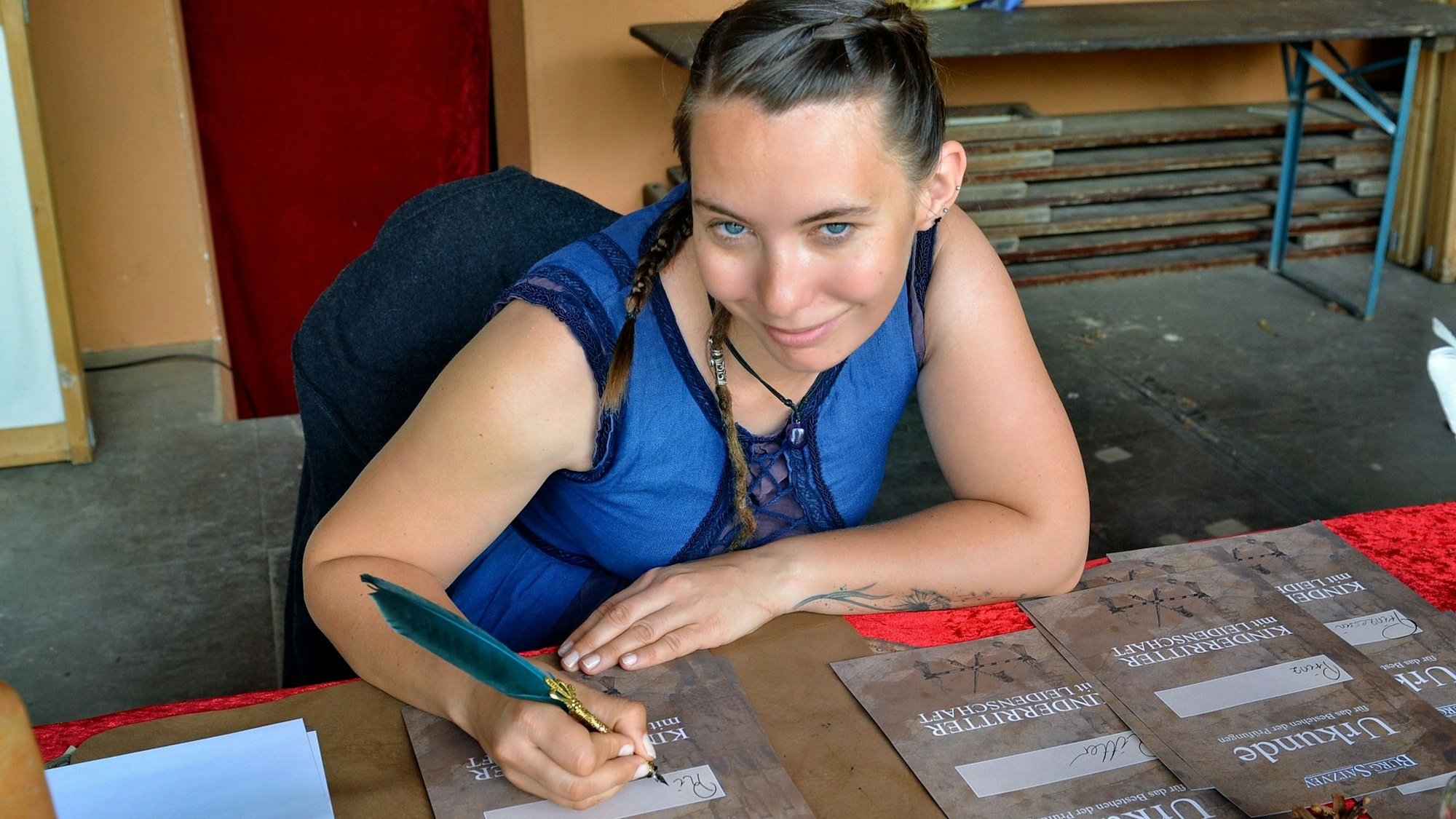 Schreiberin Toni sitzt an einem Tisch und füllt mit einer Schreibfeder eine Urkunde aus.