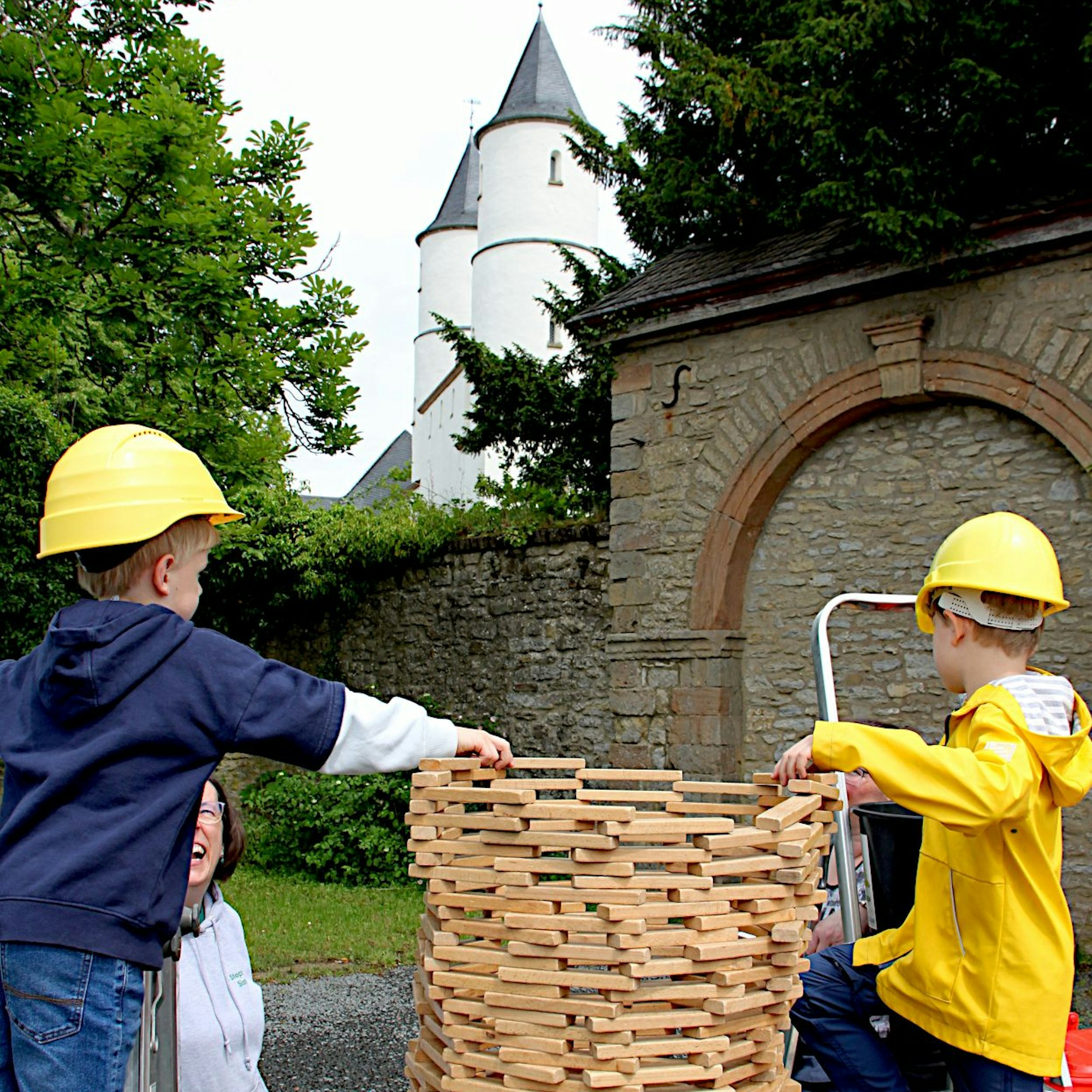 Zwei Jungen mit gelben Bauarbeiter-Helmen stapeln Klötzchen zum Turm.