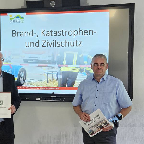 Ingo Pfennings (l.) und Wolfgang Fuchs stehen vor einem Bildschirm mit einer Fotocollage zum Brand-, Katastrophen- und Zivilschutz.