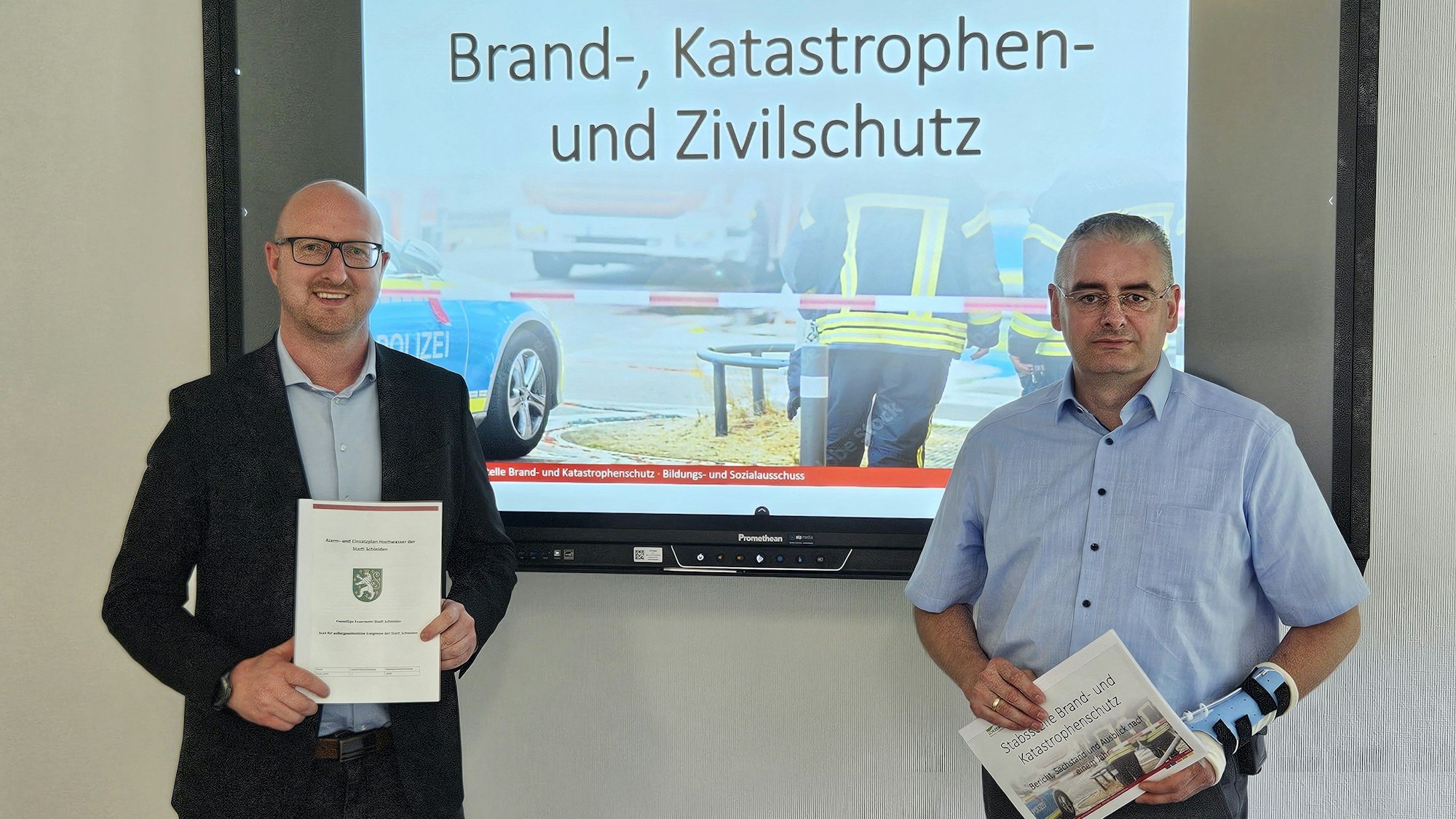 Ingo Pfennings (l.) und Wolfgang Fuchs stehen vor einem Bildschirm mit einer Fotocollage zum Brand-, Katastrophen- und Zivilschutz.