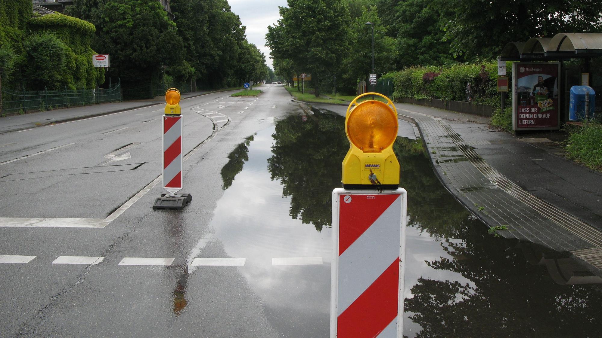 Ein See nach dem Unwetter bildet sich am Straßenrand. Drumherum stehen Warnbaken.