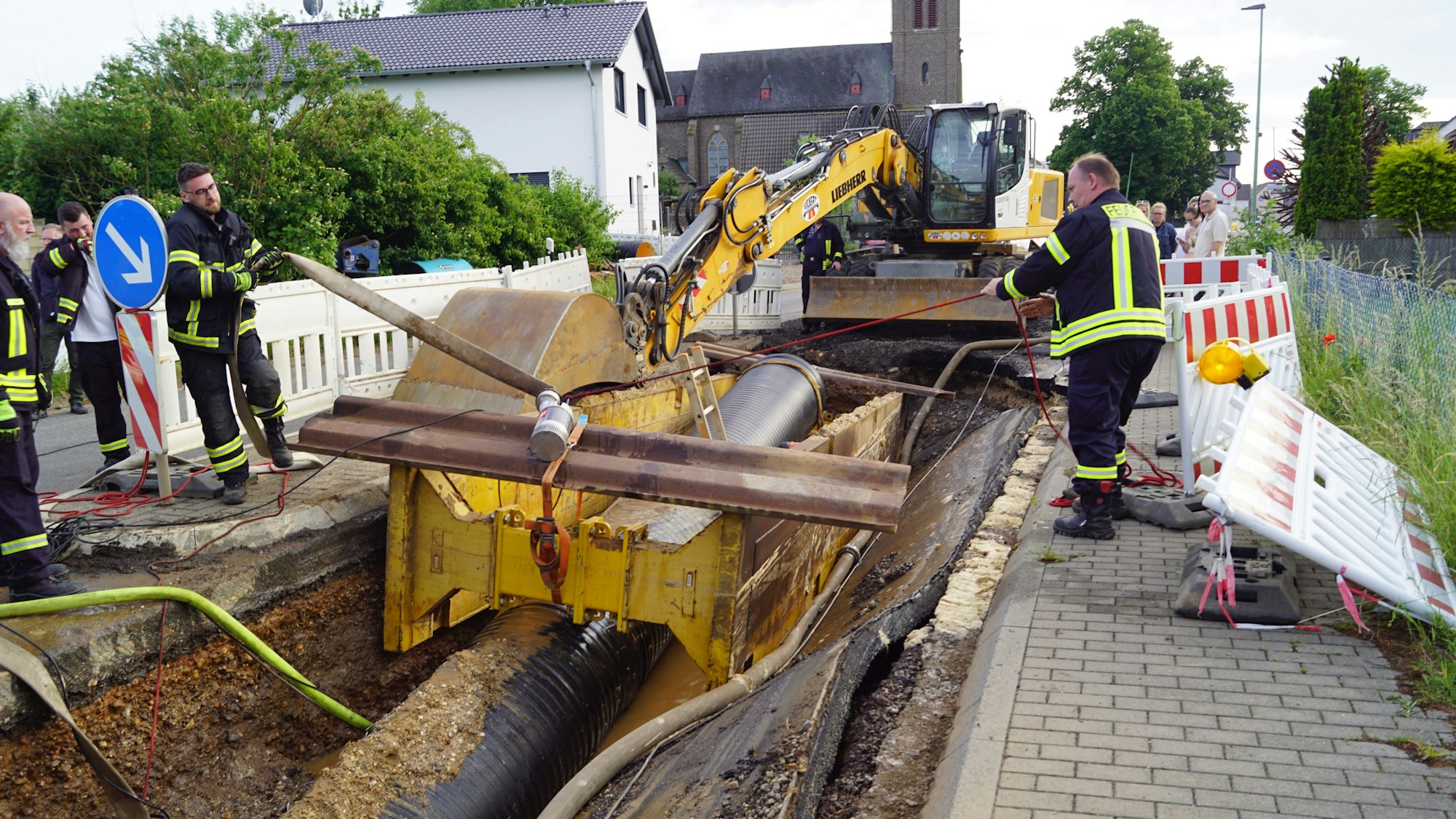 Feuerwehrleute stehen an der Baustelle mit einem hochgedrückten Rohr.