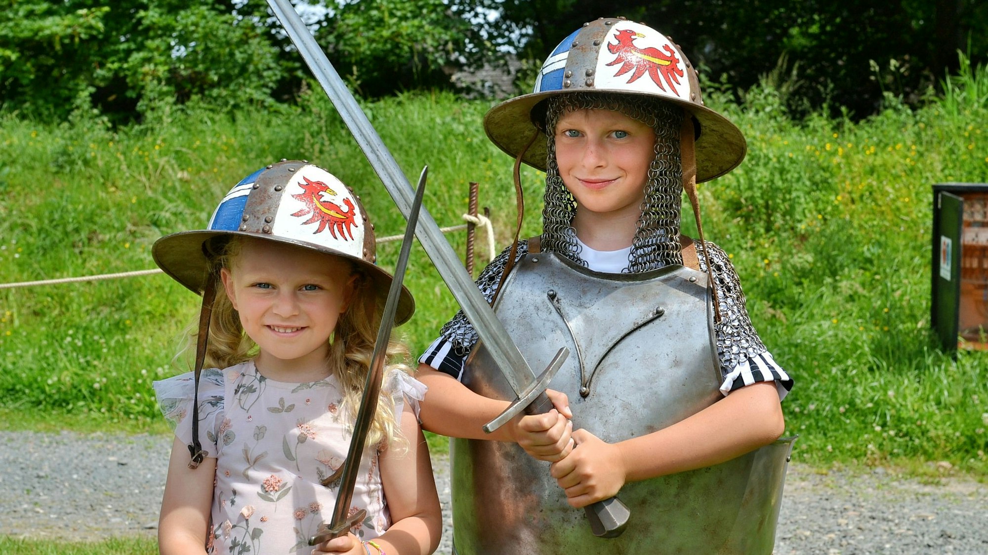 Ein Junge und ein Mädchen mit Schwertern und Helmen stehen nebeneinander.