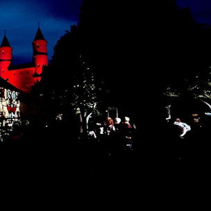 Auf dem langgestreckten Torbau ist eine biblische Szene in leuchtenden Farben zu sehen. Im Hintergrund werden die Zwillingstürme des Klosters rot vor dem nächtlichen Himmel angestrahlt.