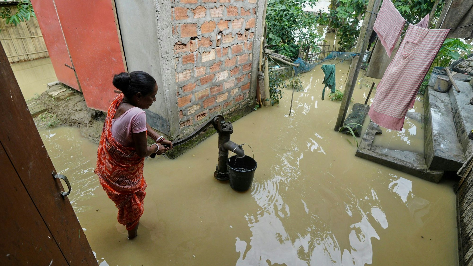 Eine Frau versucht in der überfluteten Umgebung ihres Hauses, Wasser zu sammeln.
