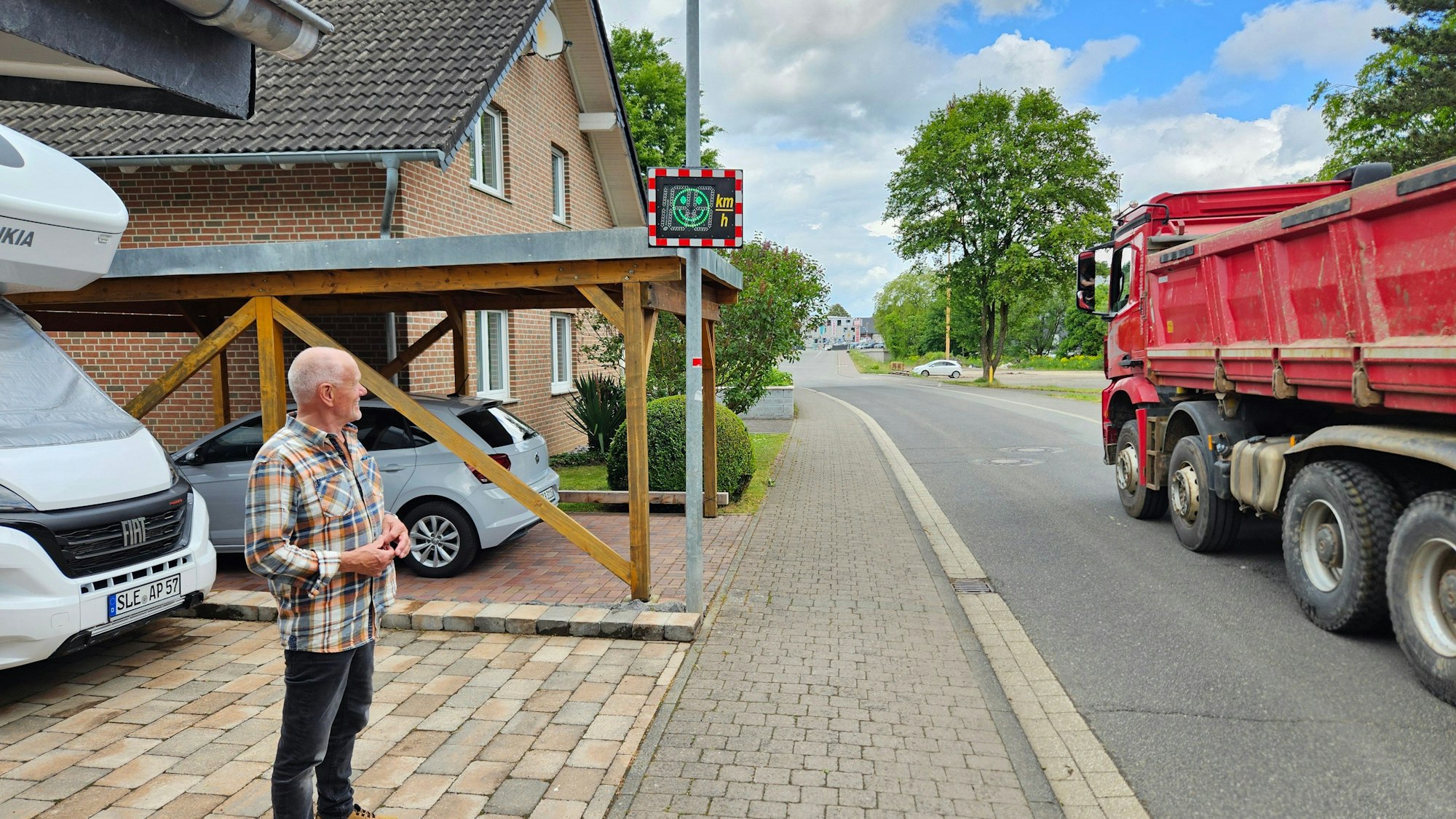 Peter Przybecki steht in seiner Einfahrt und schaut auf die Geschwindigkeitsanzeige. Ein Lkw fährt vorbei.