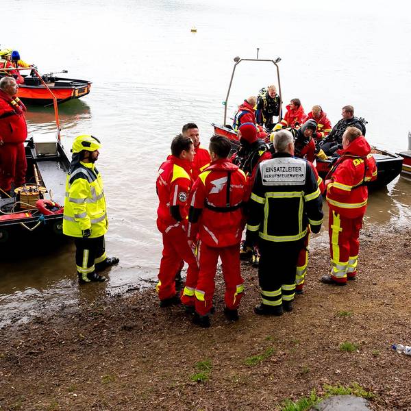 Uniformierte Männer mit Booten am Ufer der Talsperre.