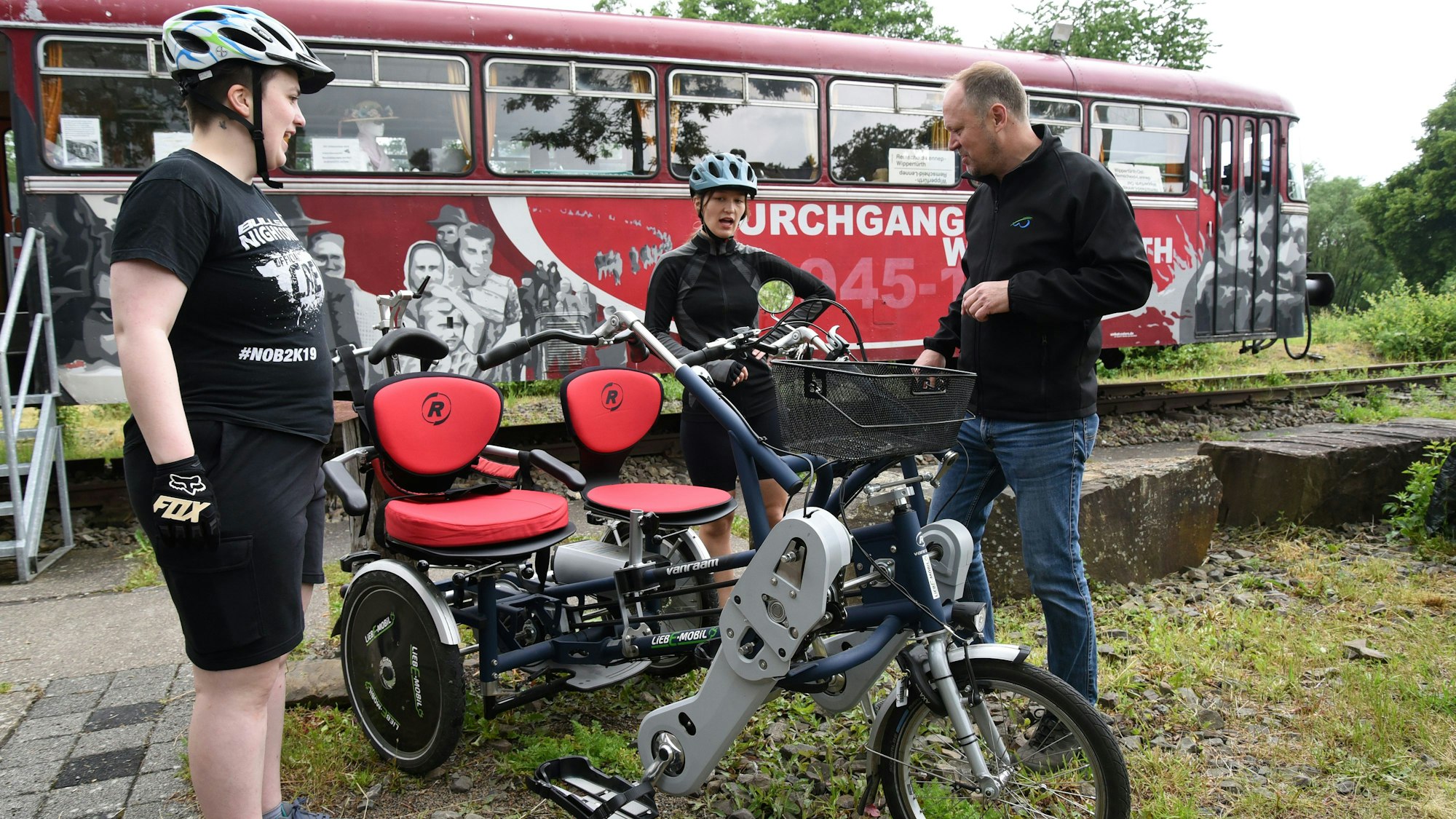 Vor einem alten Zugwagon steht ein dreirädriges Tandembike, das mehrere Besucher eines Trassen-Treffens ausprobieren.