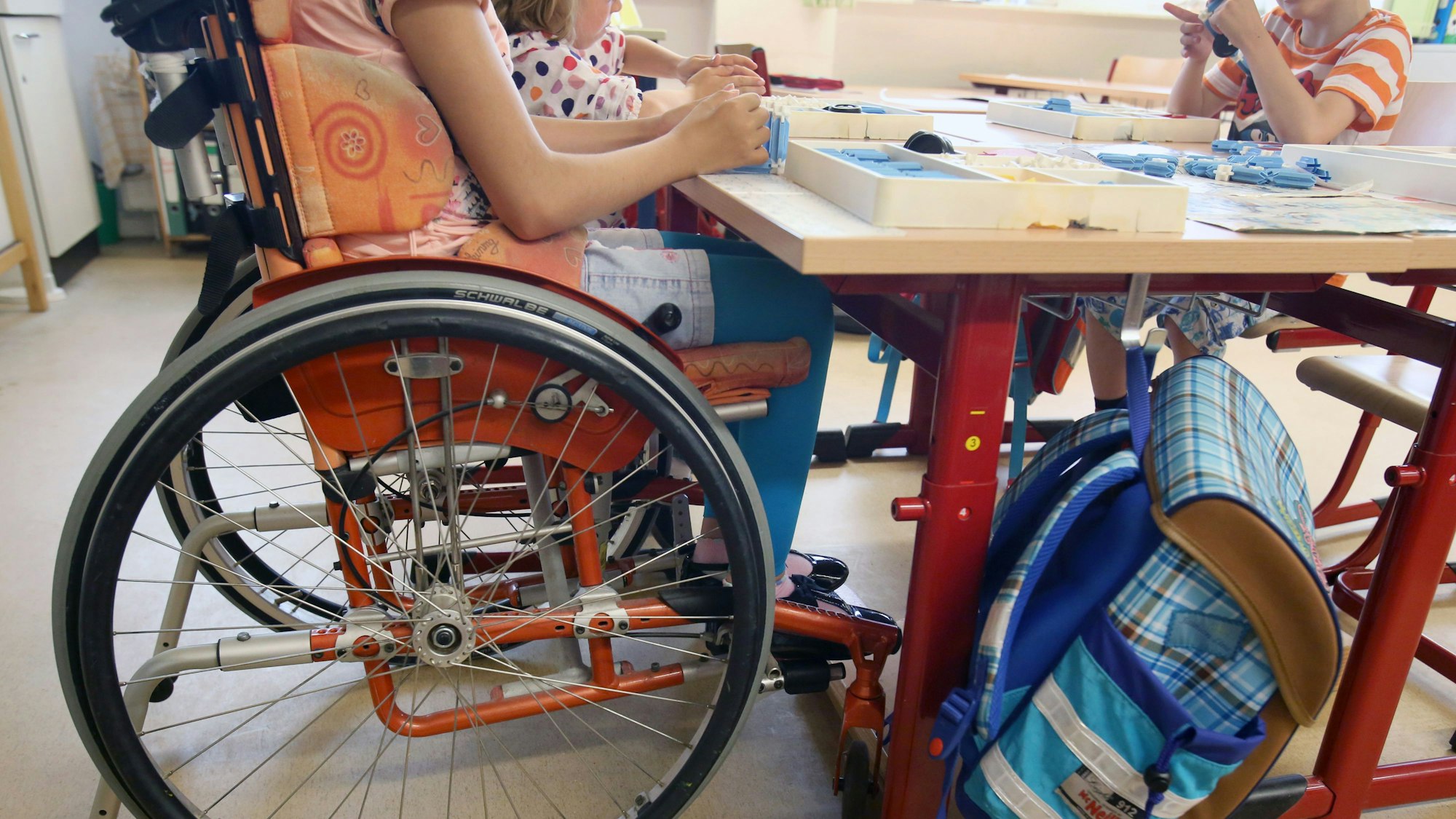 Eine Schülerin sitzt in einer 1.Klasse einer Grundschule im Klassenzimmer in ihrem Rollstuhl an einem Tisch. (Archivbild)