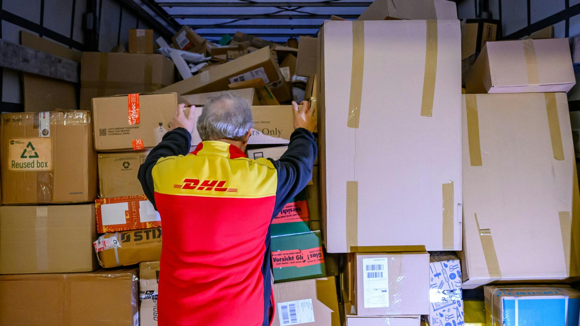 Ein Mitarbeiter bestückt im DHL-Paketzentrum den Laderaum eines Lkw mit Päckchen und Paketen.