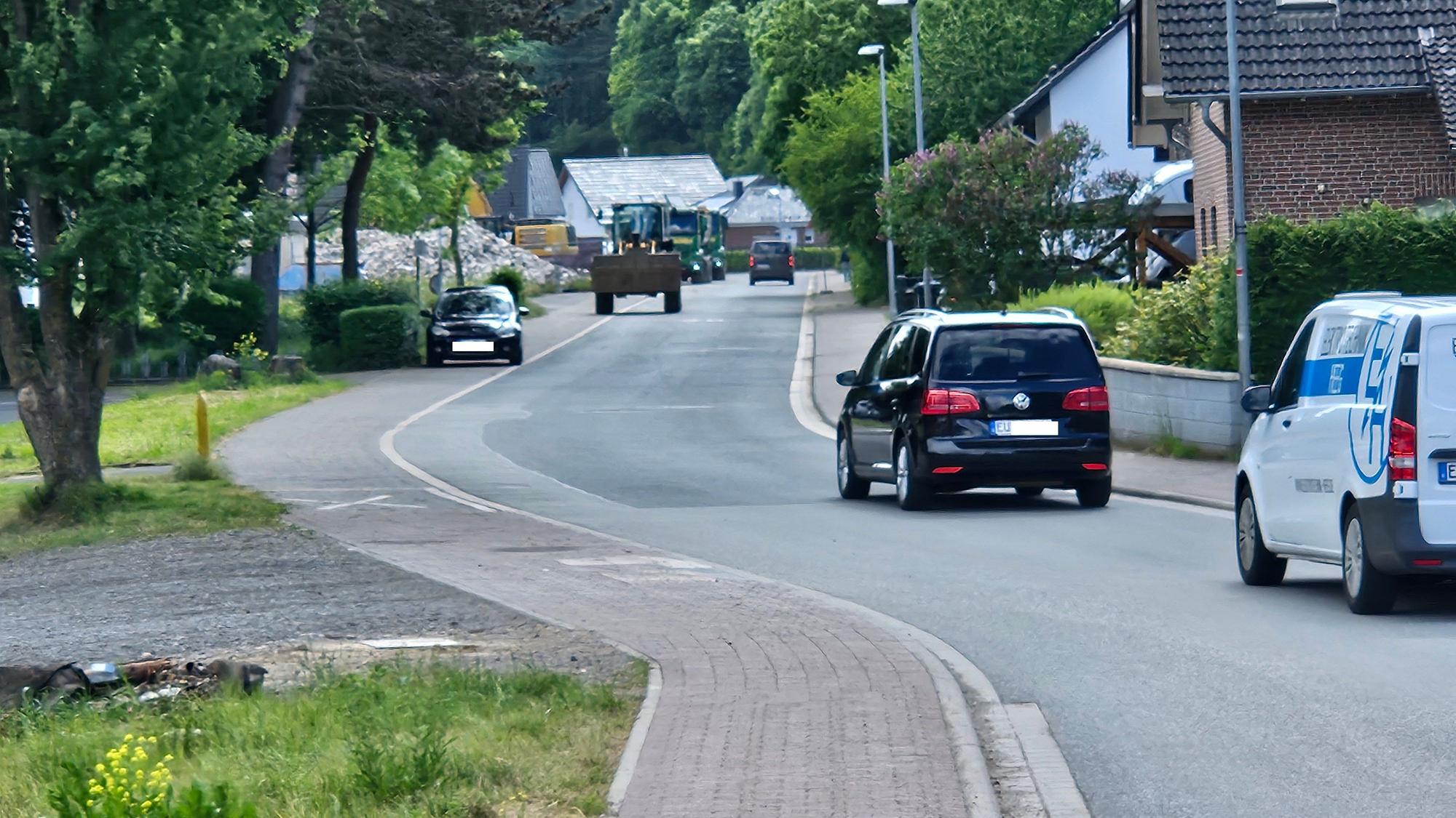 Auf einem geraden Straßenstück fahren mehrere Autos und eine Raupe.