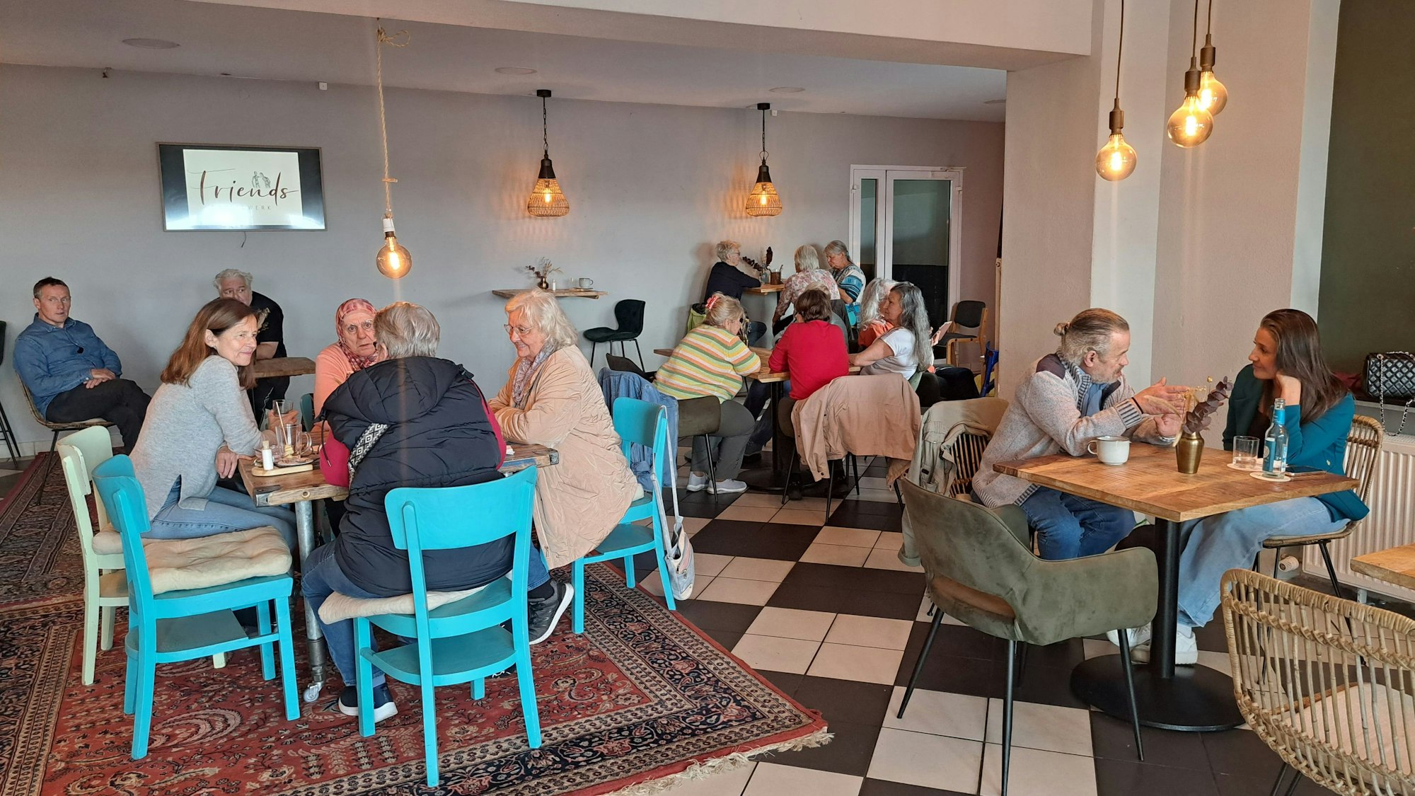 An mehreren Tischen sitzen Menschen zusammen und unterhalten sich.