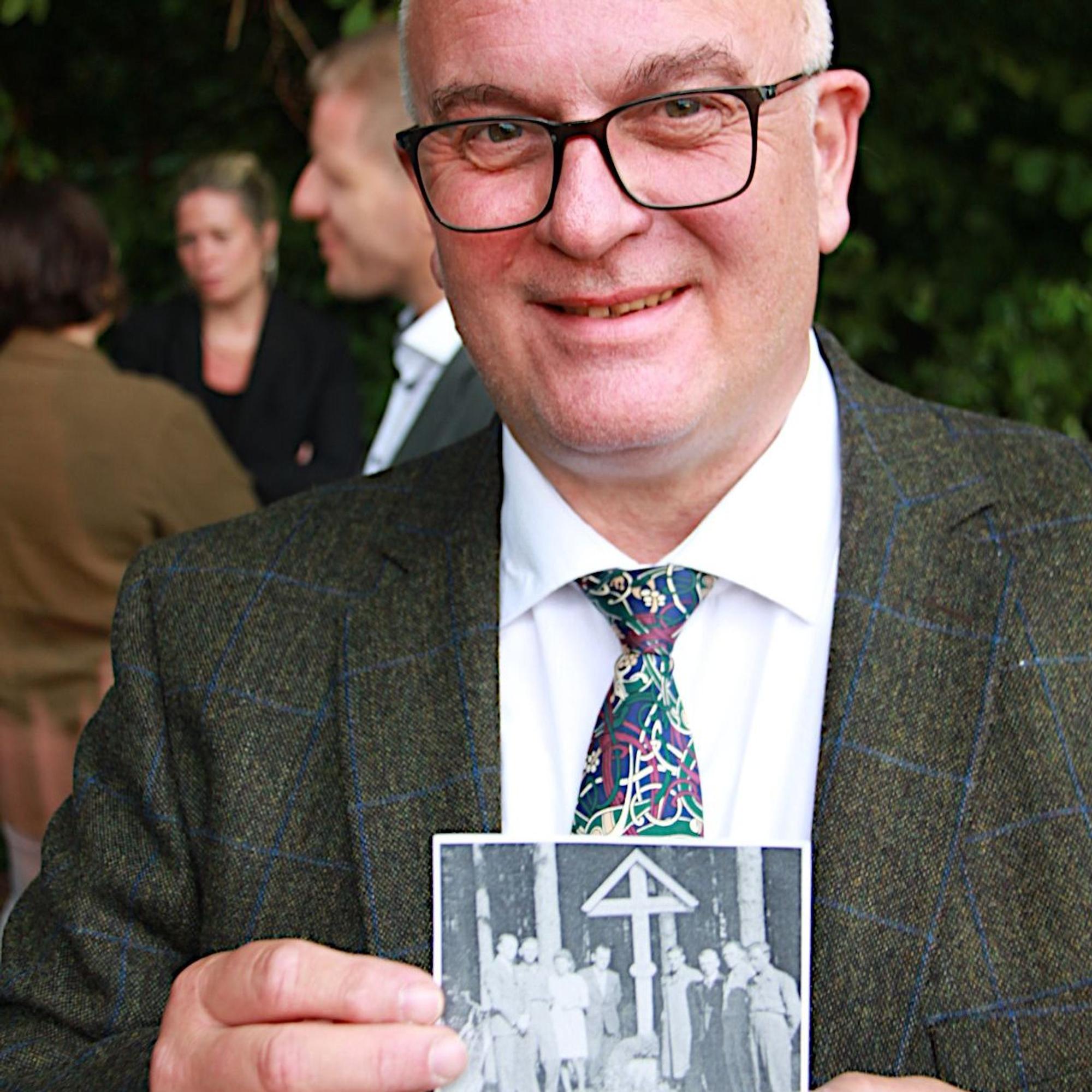 Der Lehrer zeigt ein Foto, das die Errichtung des nach Kriegsende errichteten Kreuzes zeigt.