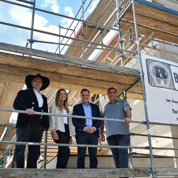 Auf dem Gerüst eines Neubaus stehen Markus Wellens, Leoni Vogel, Bürgermeister Sacha Reichelt und Projektleiter Roman Engel nebeneinander und schauen herab.