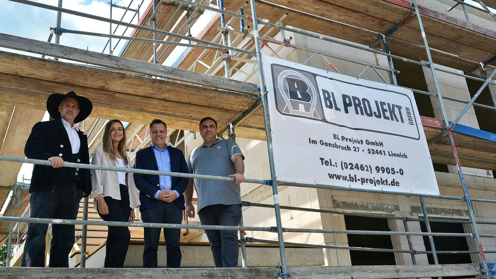 Auf dem Gerüst eines Neubaus stehen Markus Wellens, Leoni Vogel, Bürgermeister Sacha Reichelt und Projektleiter Roman Engel nebeneinander und schauen herab.