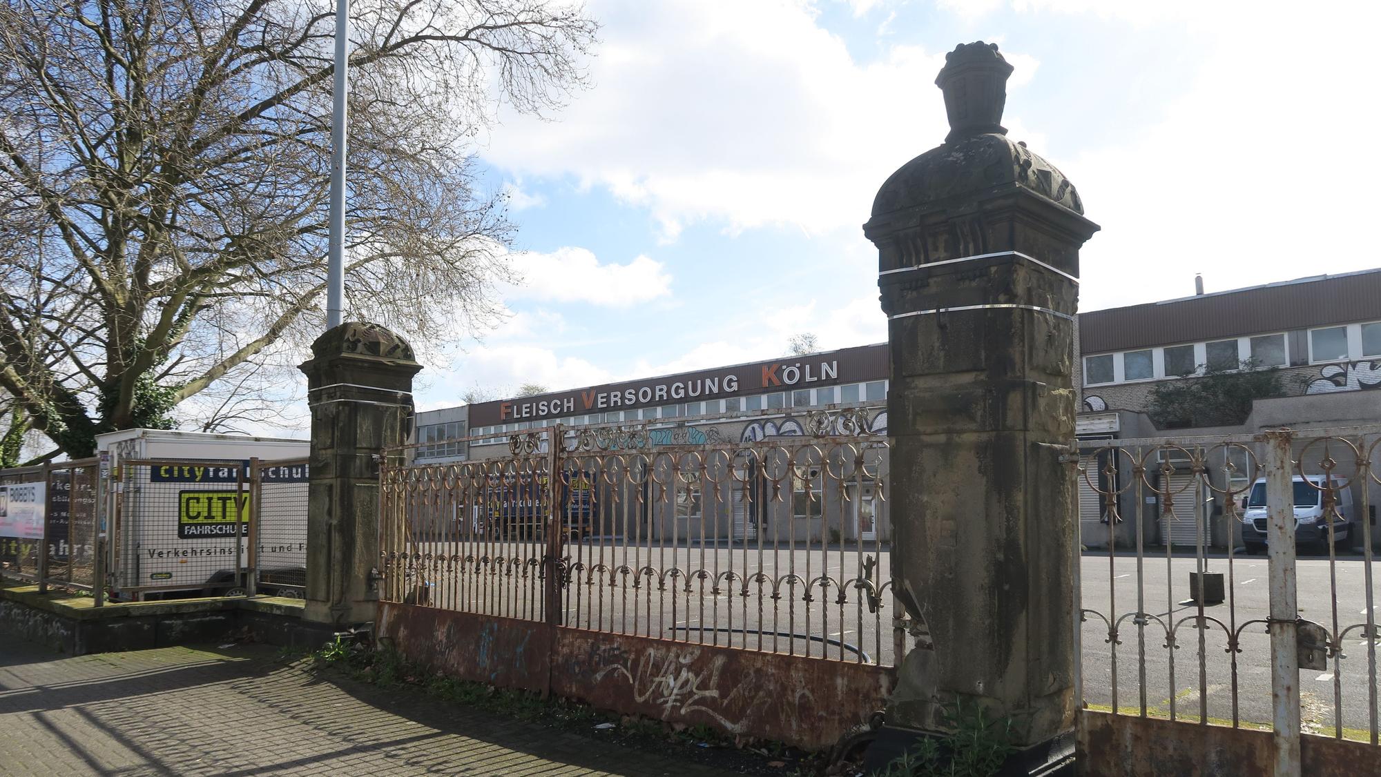 Ein großes Tor mit weitläufigen Hallen dahinter ist zu sehen. Es handelt sich um das ehemalige Gelände des Kölner Schlachthofs.