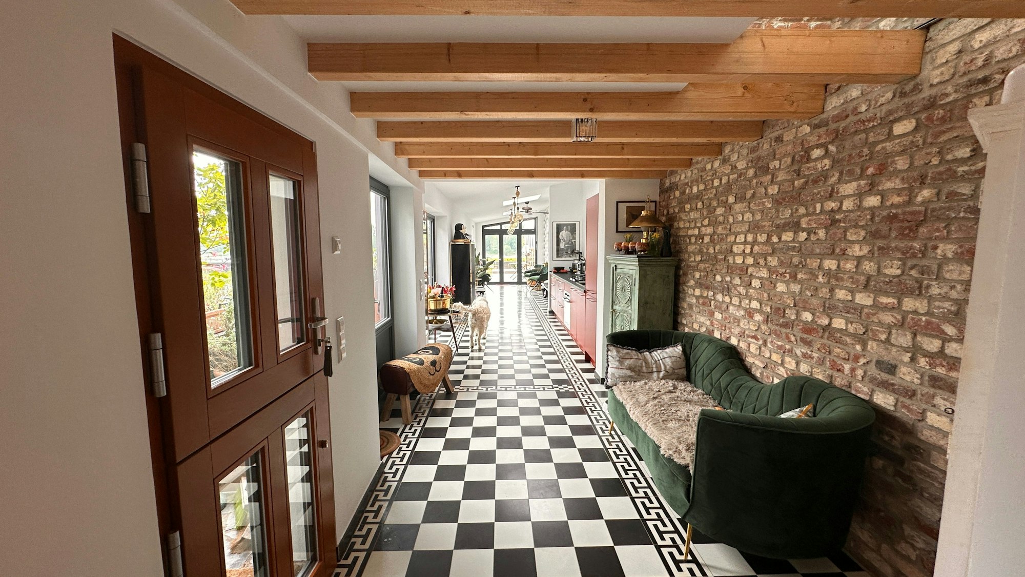 Ein schwarz-weißer Steinboden, Holzbalken an der Decke und eine Natursteinwand dominieren einen sehr langen Raum, der in die Küche des Hauses und den Wohn-/ Essbereich führt.