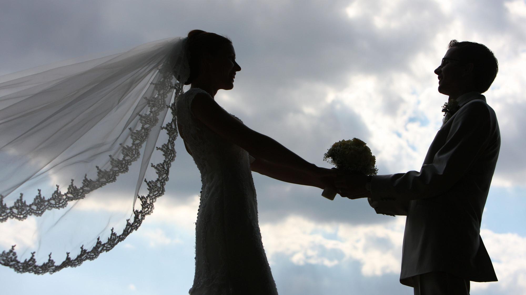 Die Silhouette eines frisch vermählten Hochzeitspaares zeichnet sich im Gegenlicht ab.