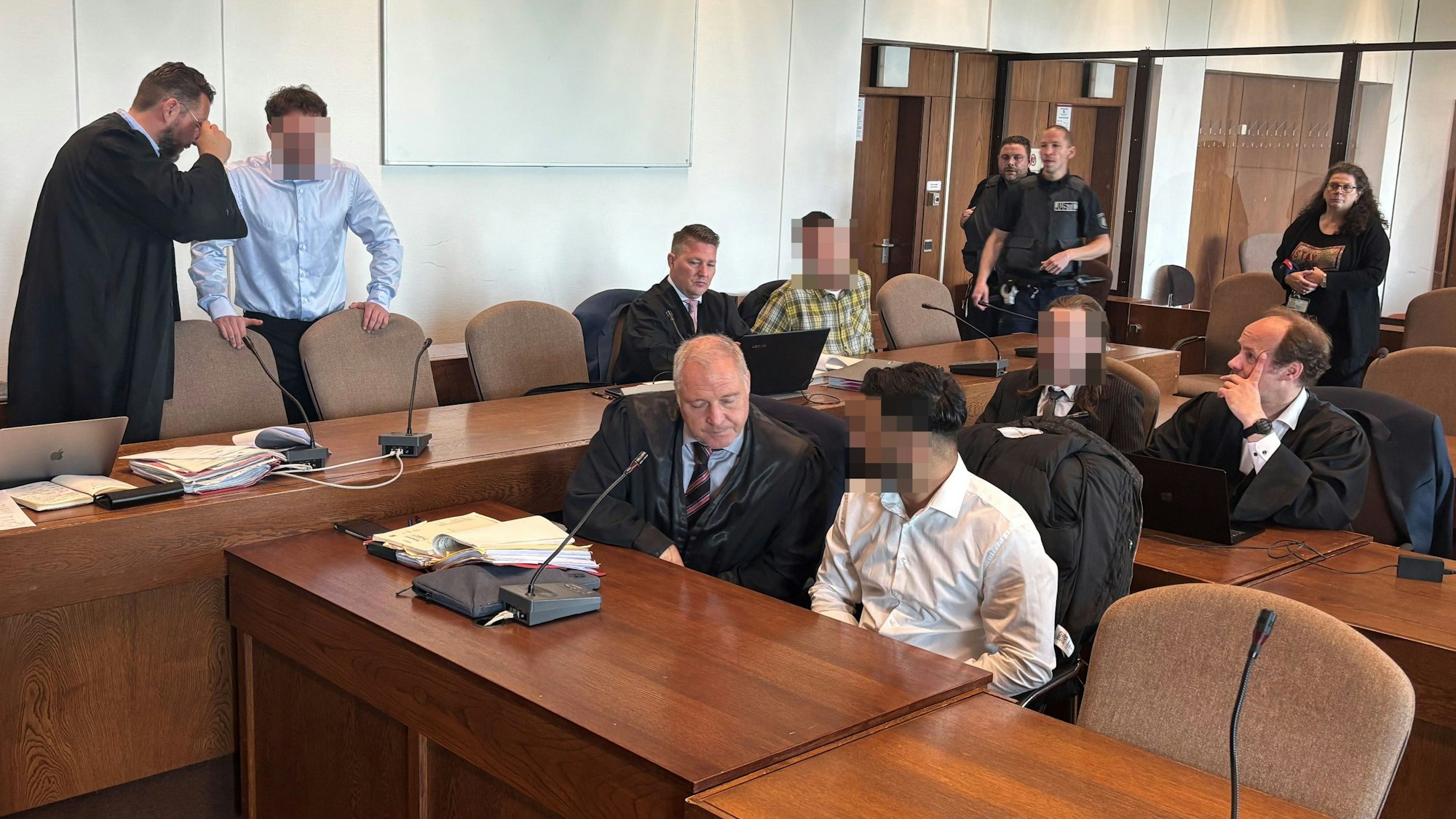 Das Bild zeigt einen Gerichtssaal mit den vier Angeklagten und ihren Verteidigern.