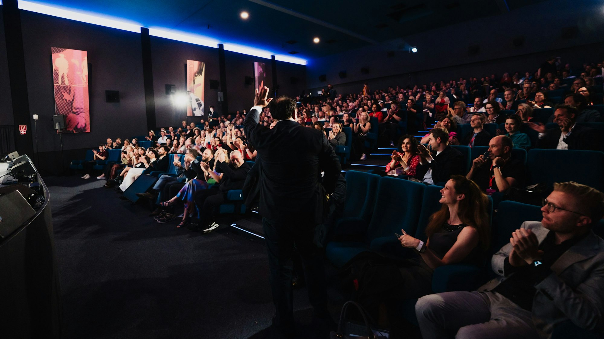 NRW-Medienminister Nathanael Liminski steht in einem Kinosaal vor einem applaudierenden Publikum.