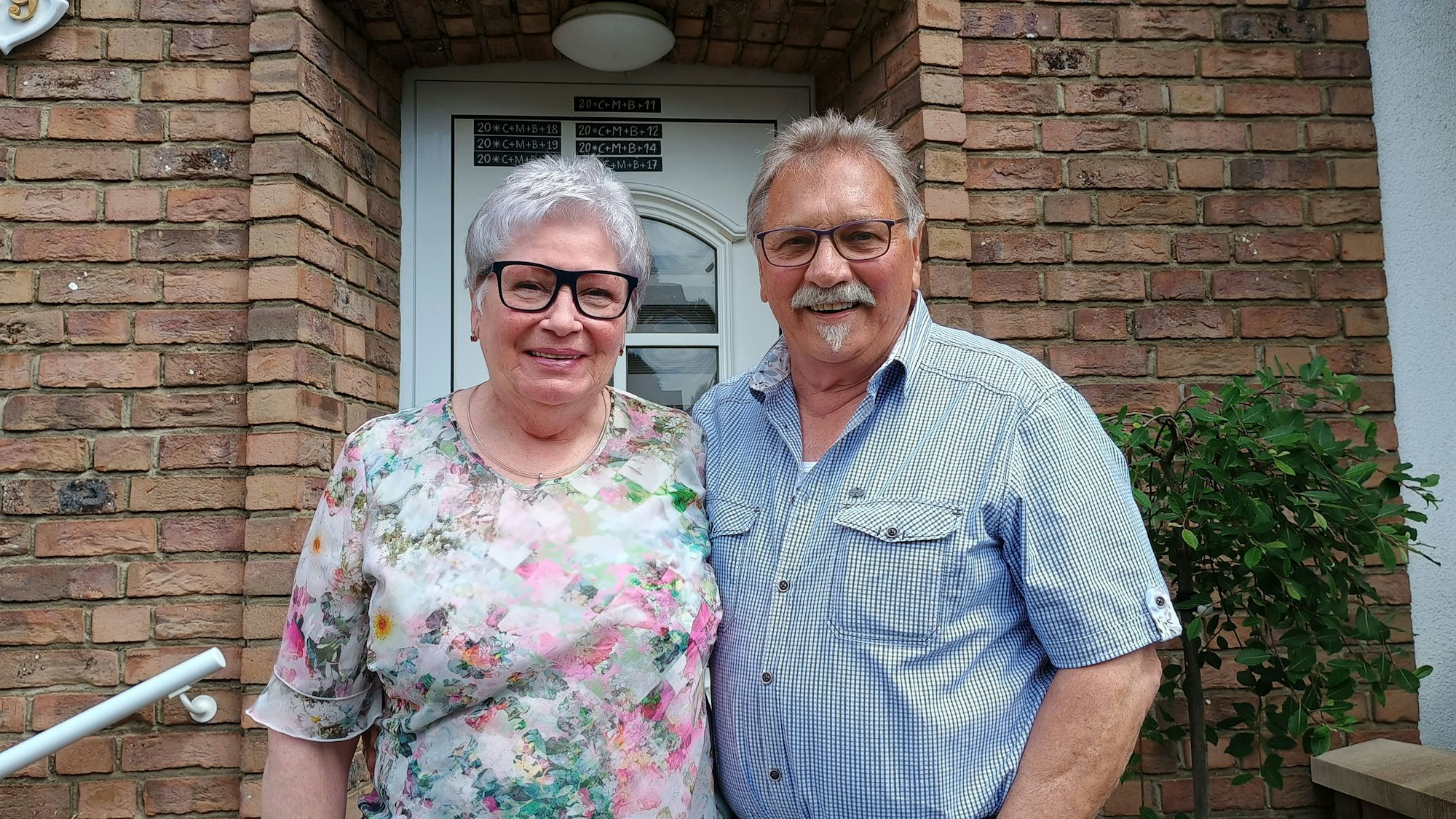 Klara Bloch trägt eine Bluse mit Blumen, ihr Mann ein hellblaues Hemd. Sie stehen vor ihrem Haus und lächeln in die Kamera.