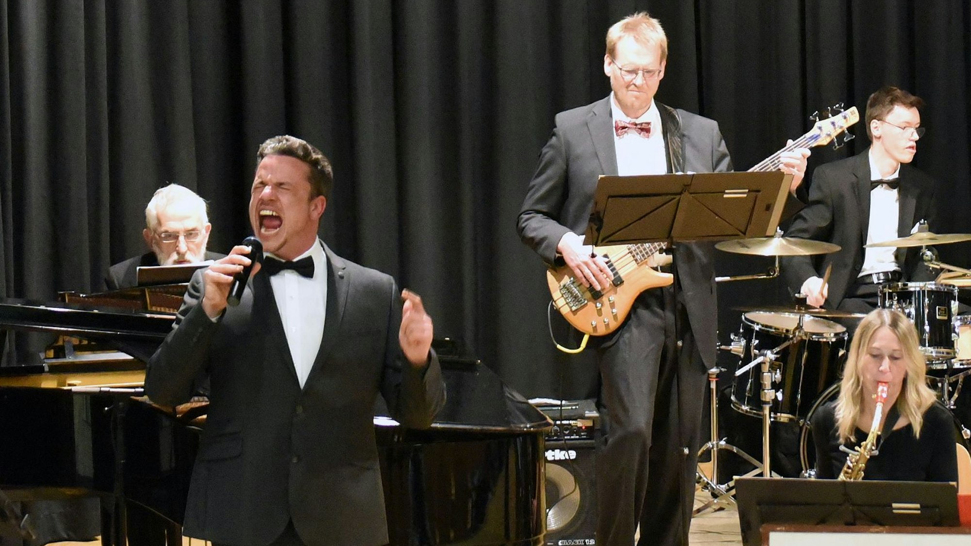 Ein Sänger im Smoking mit Fliege vor Orchester.