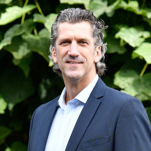 Auf dem Bild ist ein Portrait des Niederlassungsleiter der Deutschen Marktgilde zu sehen, er trägt einen dunklen Anzug und eine Krawatte.