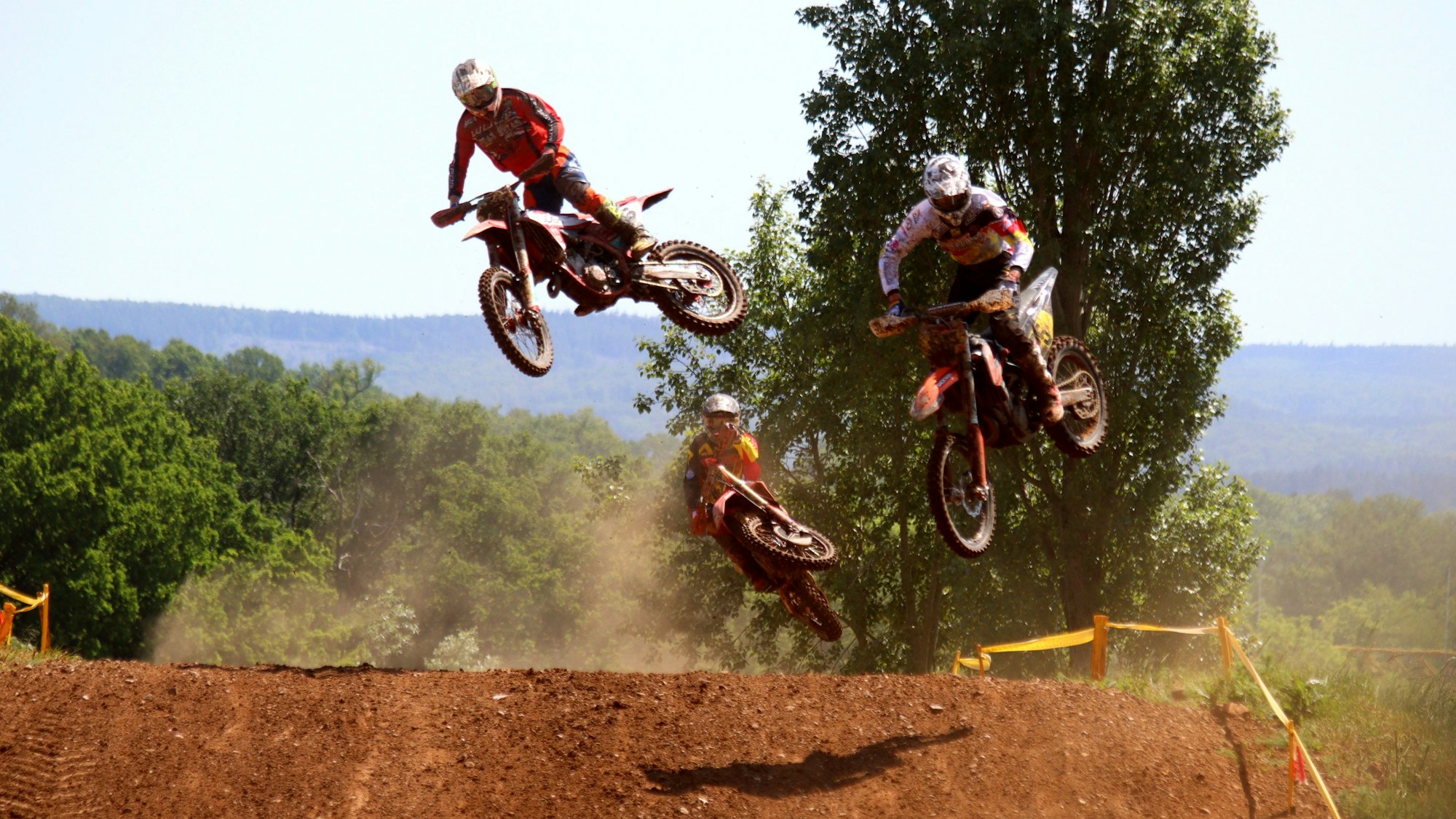 Drei Motocross-Maschinen springen über die Kuppe eines Hügels auf der Strecke in Satzvey.