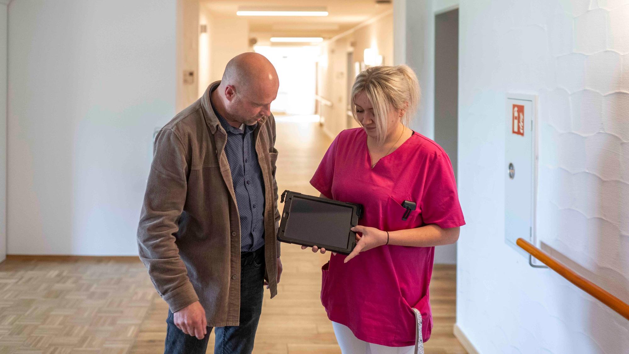 Heimleiter Lars Hammer und Melanie Klein stehen auf einem Flur im Kreuser-Stift und schauen auf ein Tablet, das Klein in den Händen hält.