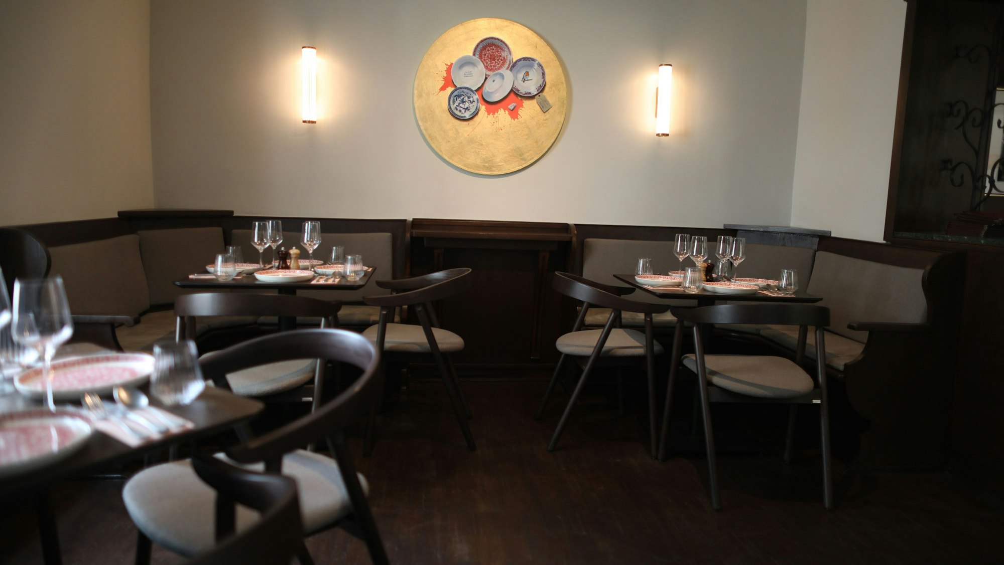 Eine Ansicht des Gastraums mit kleinen gedeckten Tischen und grau bezogenen Polstermöbeln.