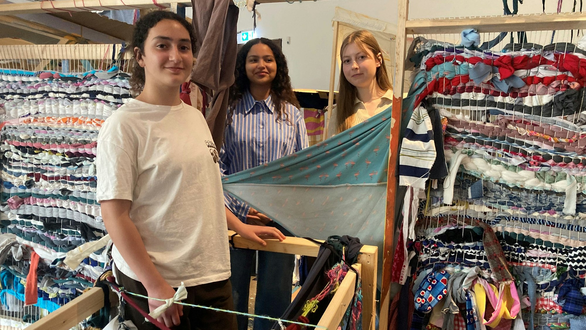 Drei Mädchen zwischen gewebten bunten Flächen.