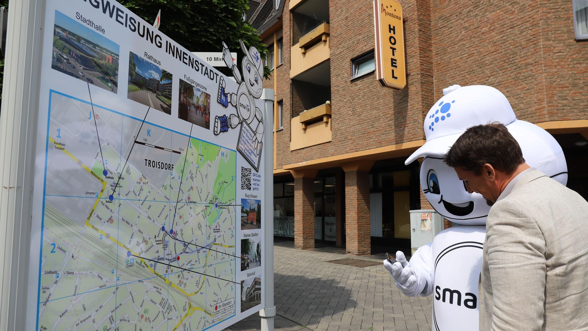 Smart City-Maskottchen SmarTa erklärt Bürgermeister Alexander Biber die App für die Entdeckungstouren.