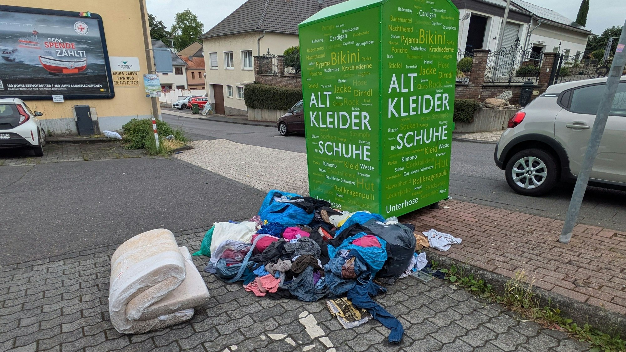 Kleider und eine alte Matratze vor einem Altkleidercontainer in Alfter-Ort.
