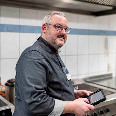 Küchenchef Timo Caspers steht in der Küche und hat ein Tablet in der Hand.