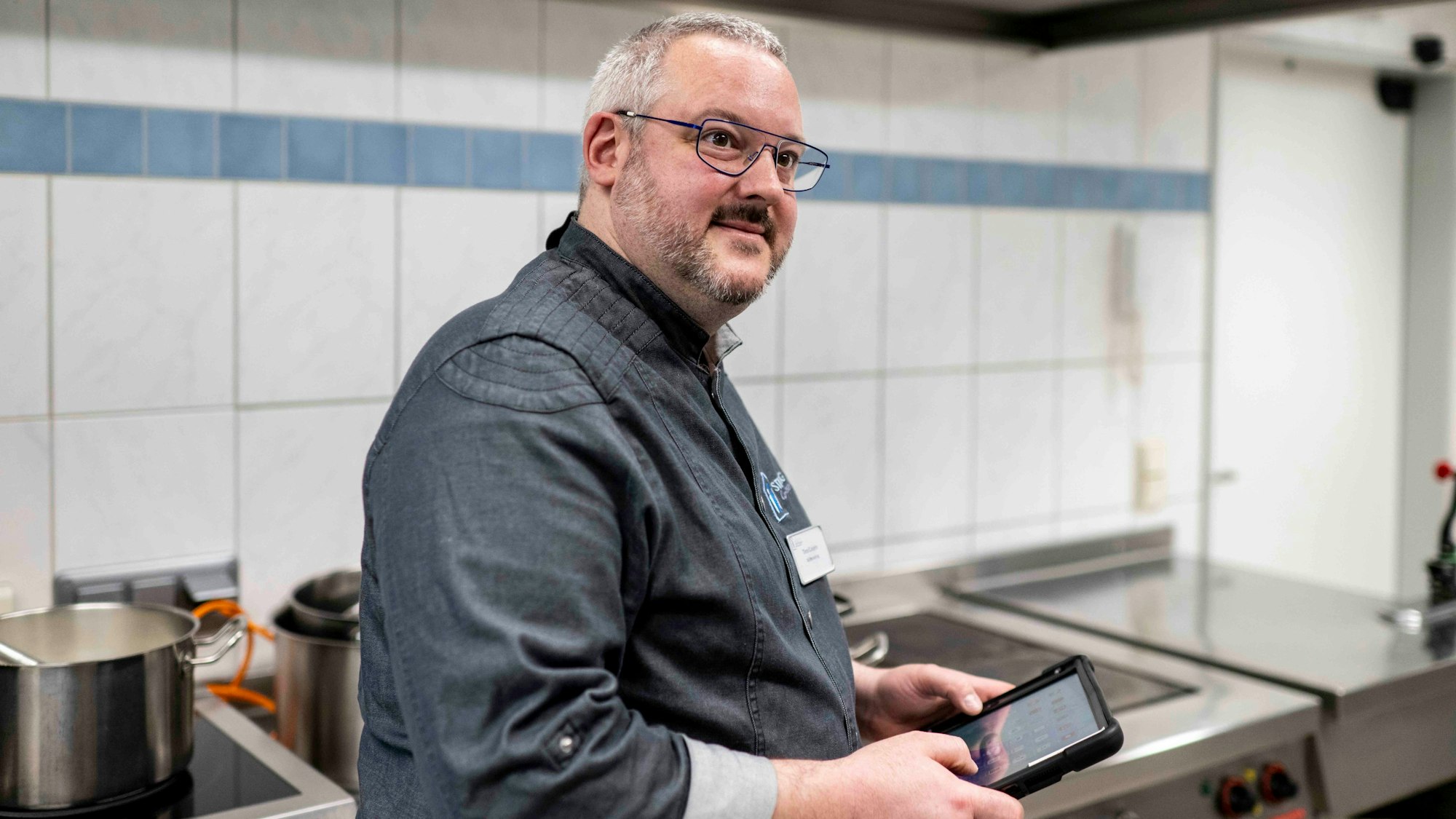 Küchenchef Timo Caspers steht in der Küche und hat ein Tablet in der Hand.