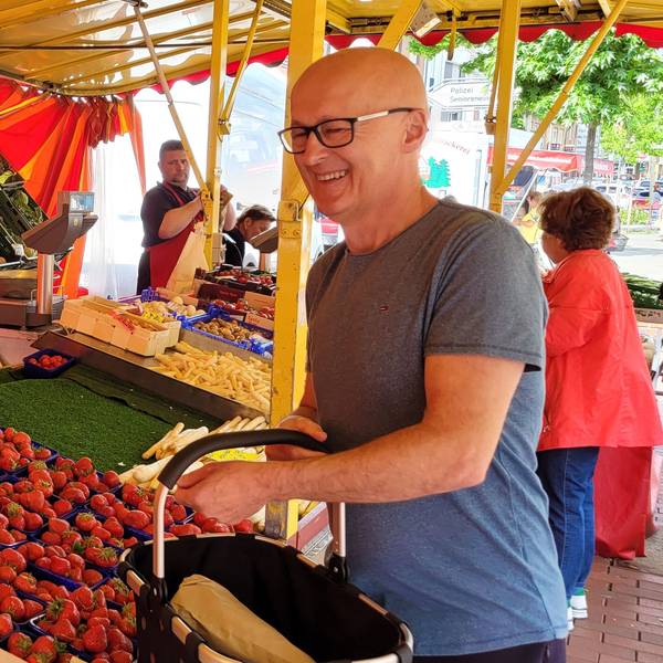 Ein Mann bedient einen Kunden auf einem Wochenmarkt, der gerade Erdbeeren gekauft hat.