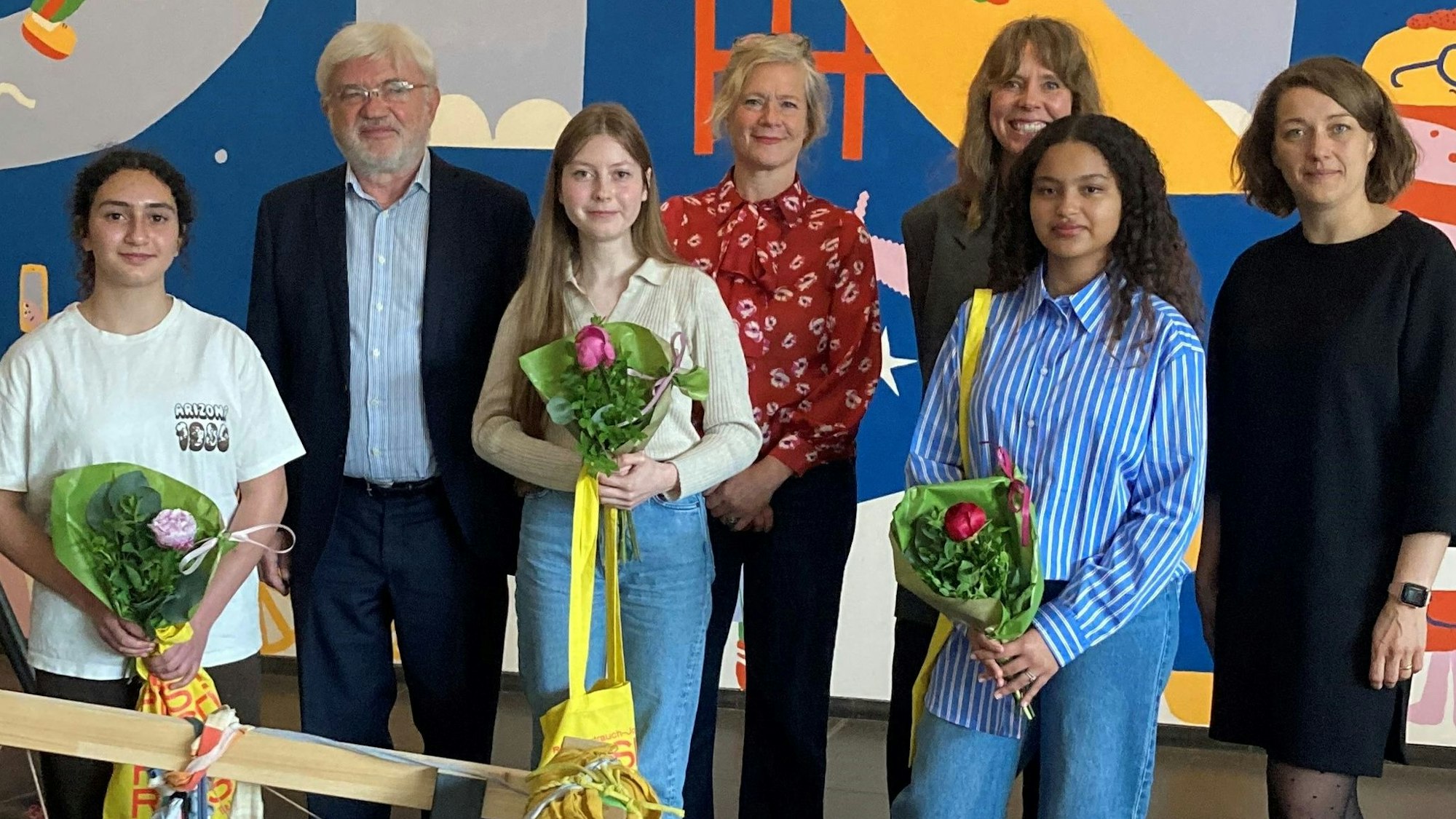 Drei Mädchen mit Blumen und vier Erwachsene.