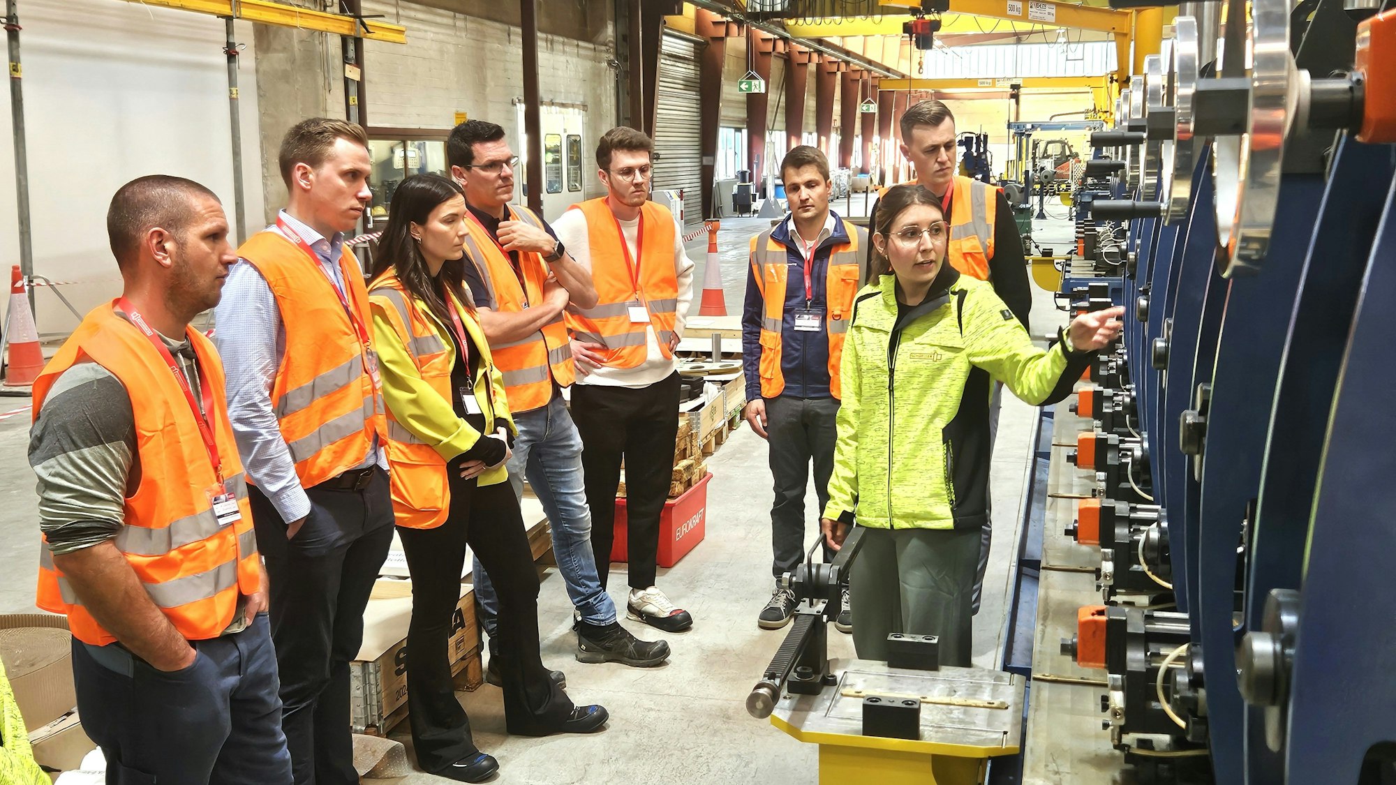 Eine Gruppe Menschen steht in Warnwesten gekleidet in einer Produktionshalle.