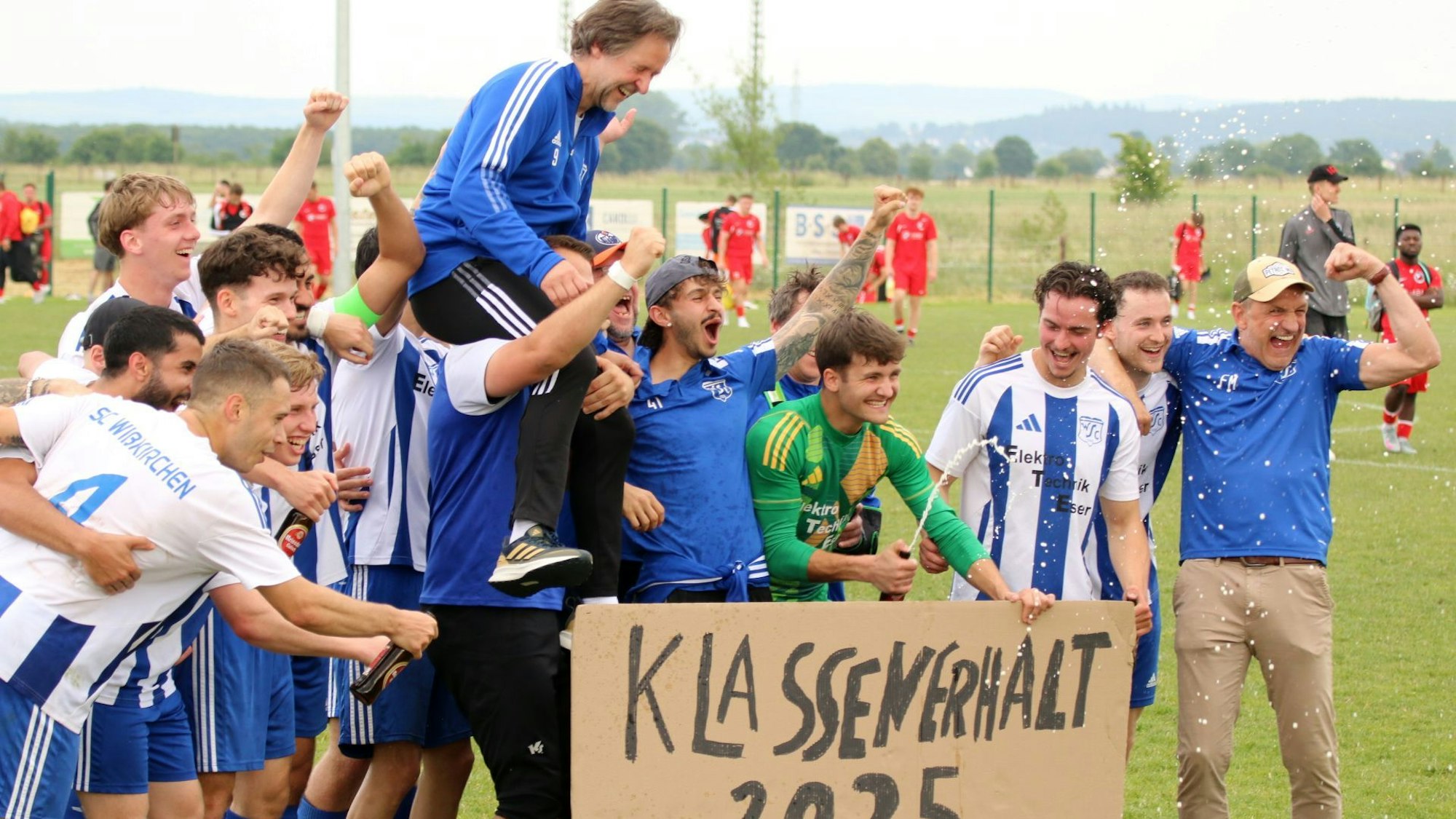 Die Wißkirchener Spieler stehen hinter einer Pappe, auf der "Klassenerhalt 2025" steht. Ihren Trainer Horst Bartz tragen sie auf Schultern.