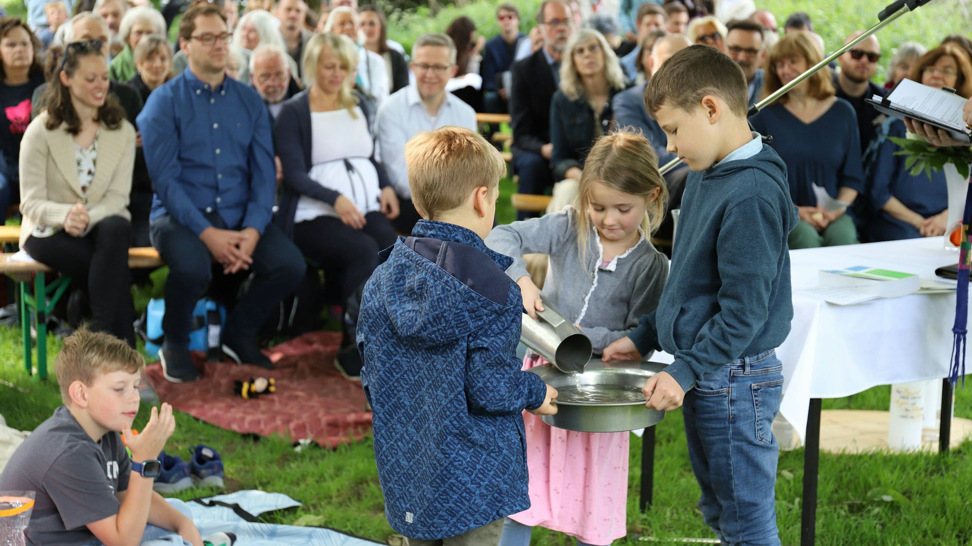 Aus einer Karaffe schüttete ein Mädchen das Wasser aus der Sieg in ein Taufbecken, das zwei Jungen hielten.