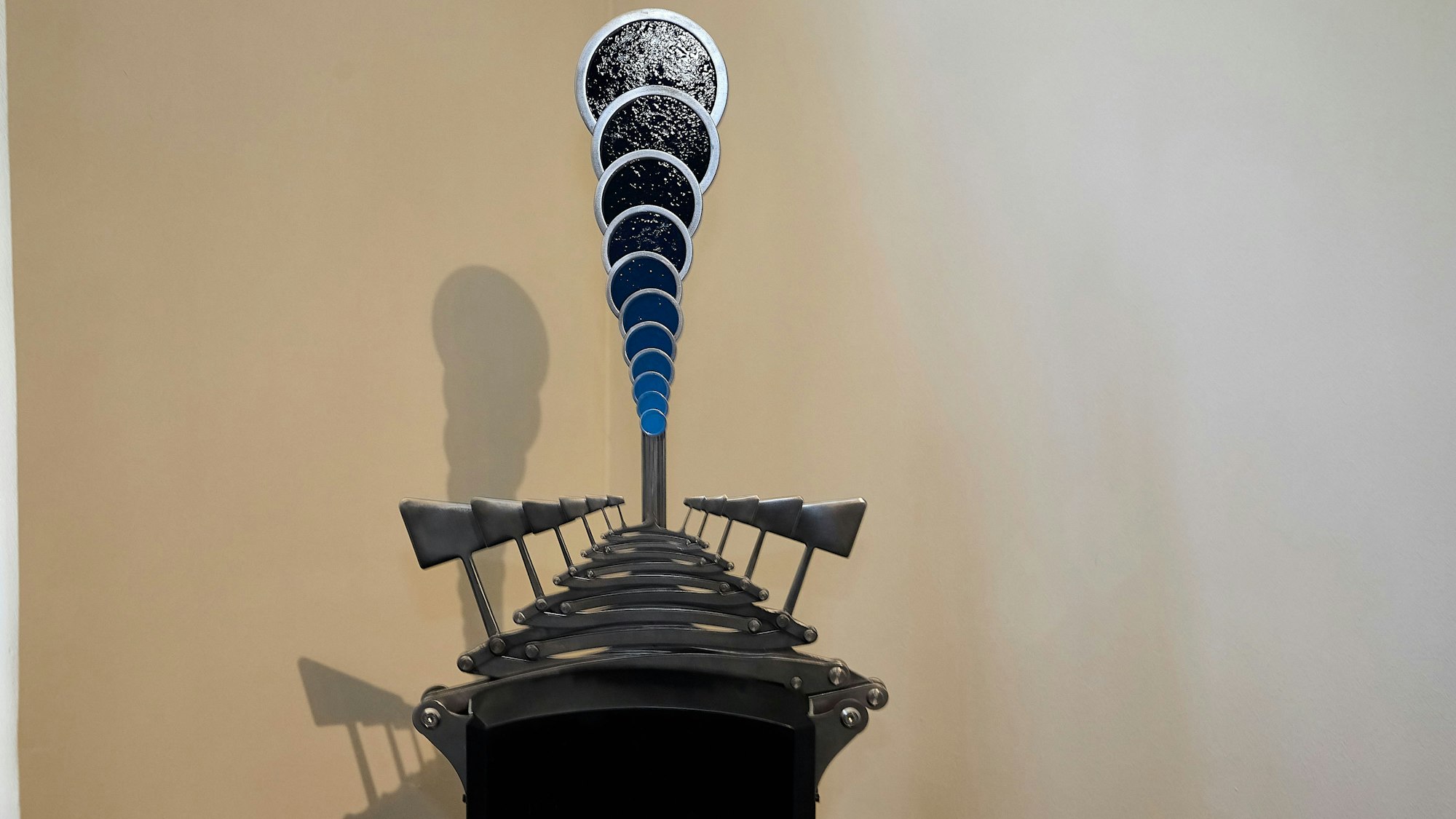 Das Bild zeigt ein Kunstwerk, das aus mehreren blauen Kreisen und Metall-Hammern besteht.