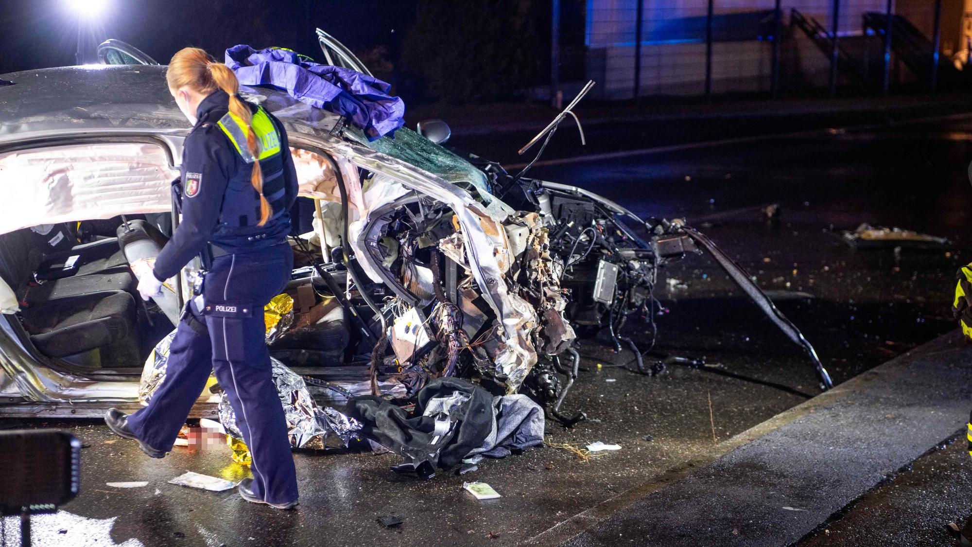 Eine Polizistin geht im Dunkeln an einem zerstörten Auto vorbei.
