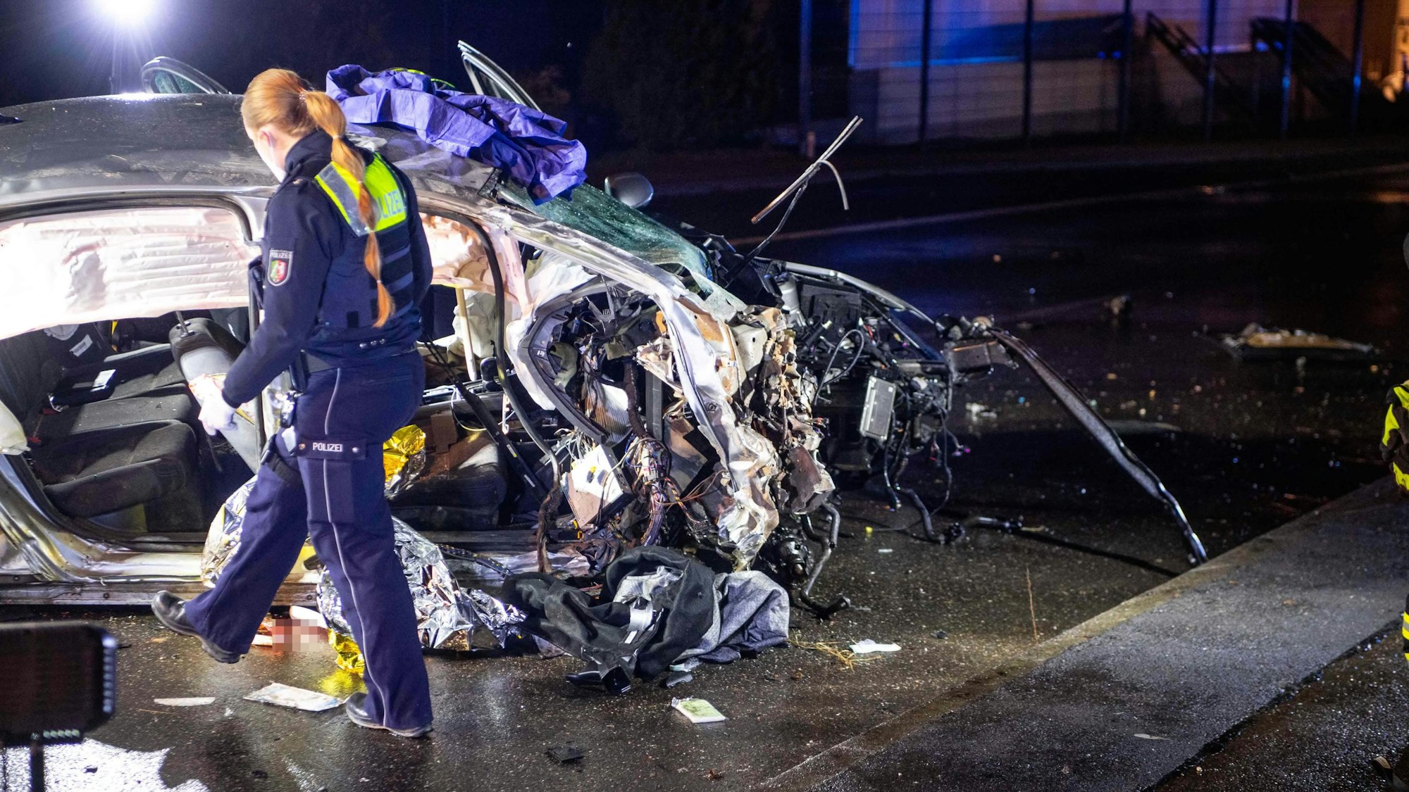 Eine Polizistin geht im Dunkeln an einem zerstörten Auto vorbei.